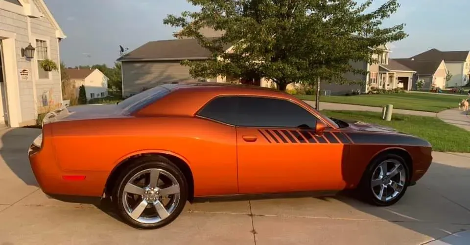 An orange dodge challenger is parked in a driveway in front of a house.