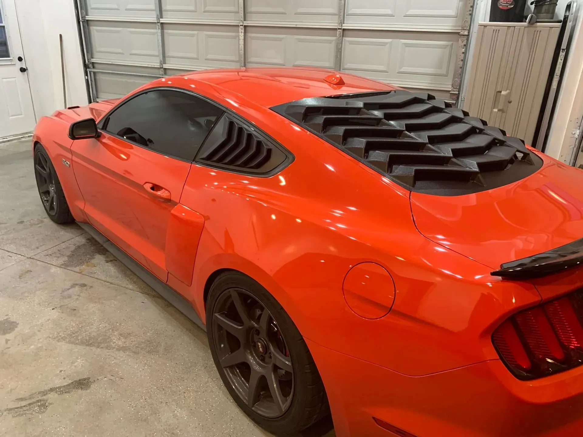 A red mustang is parked in a garage next to a garage door.