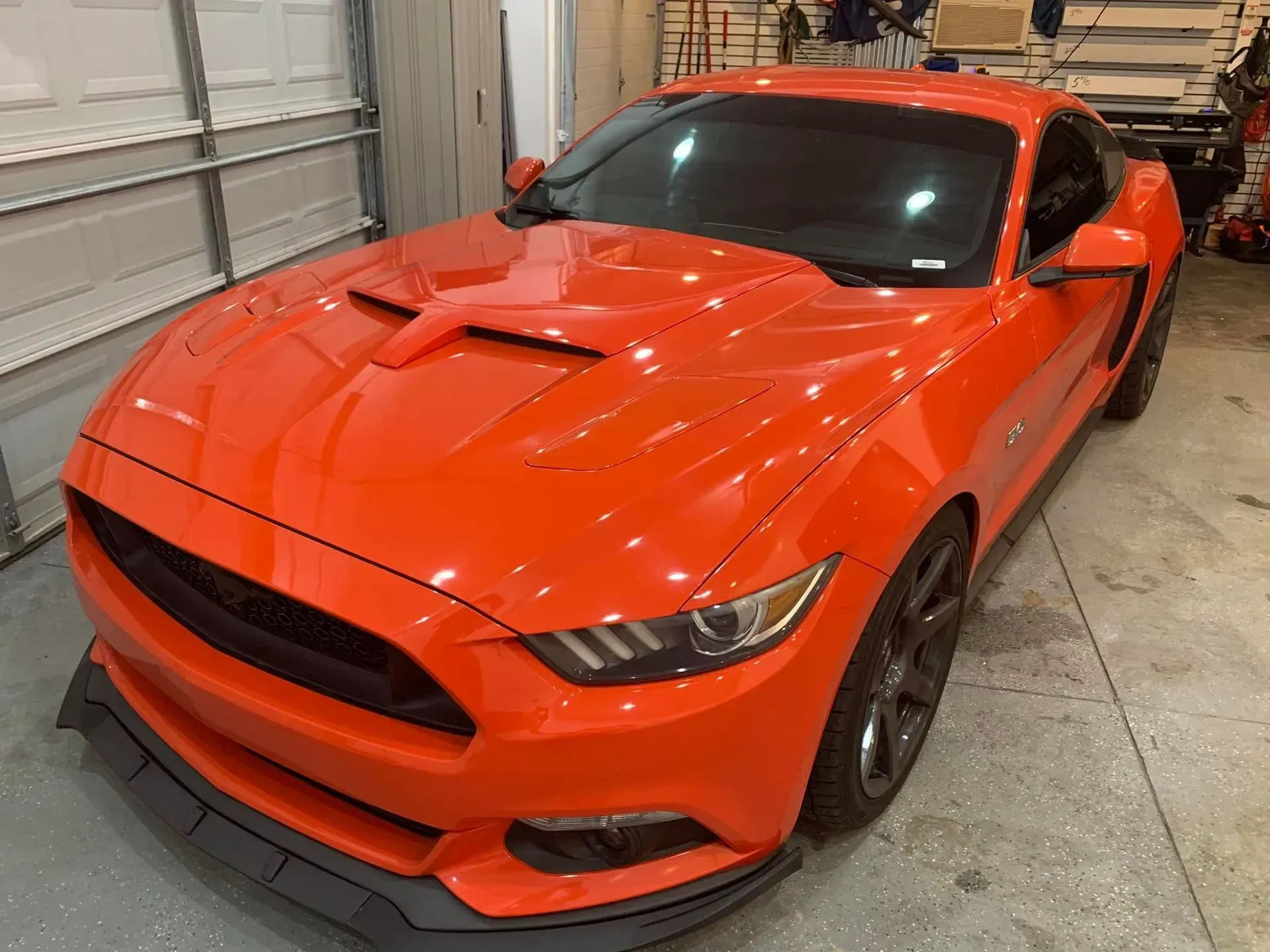An orange ford mustang is parked in a garage.