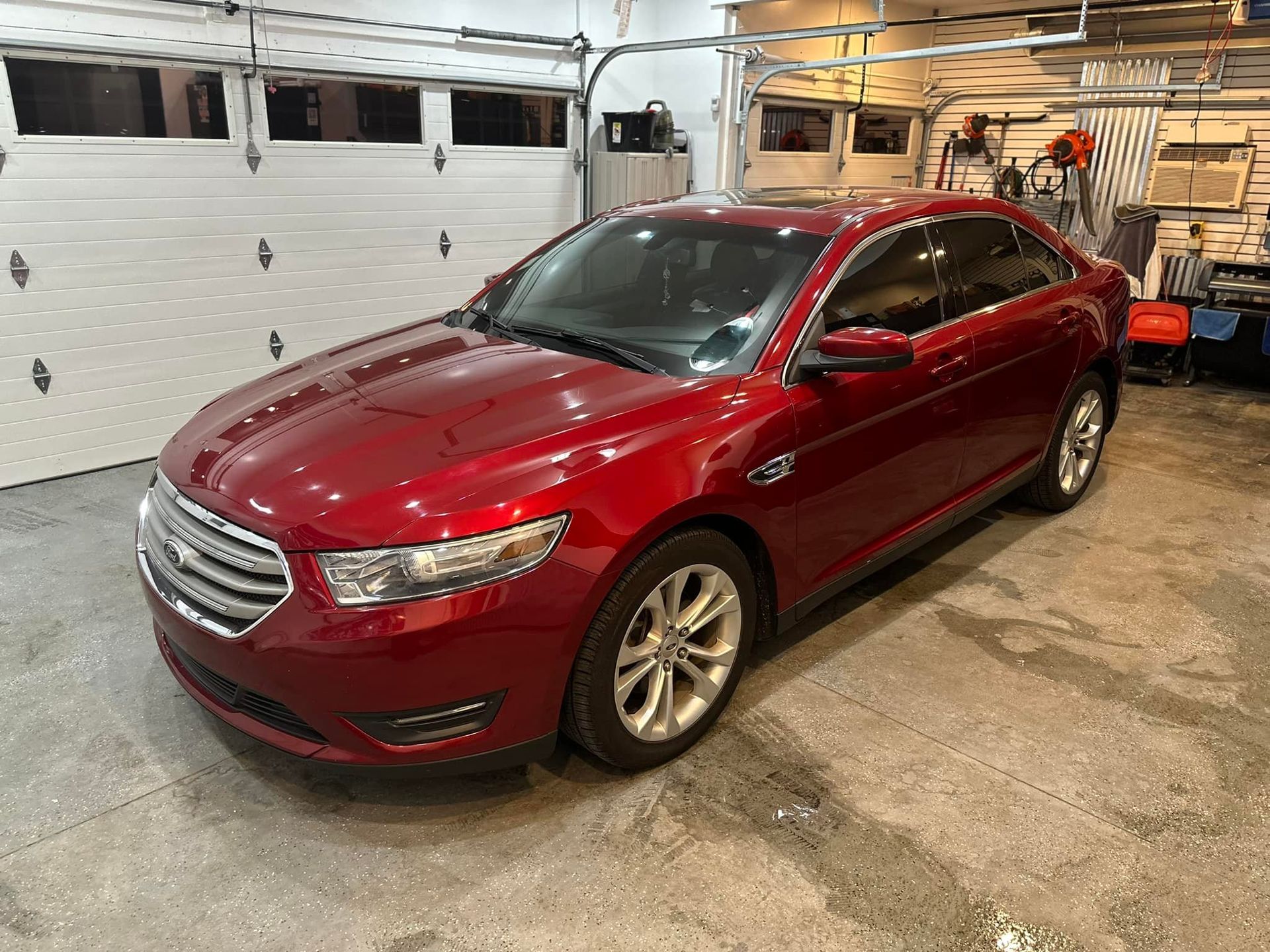 A red ford taurus is parked in a garage next to a garage door.