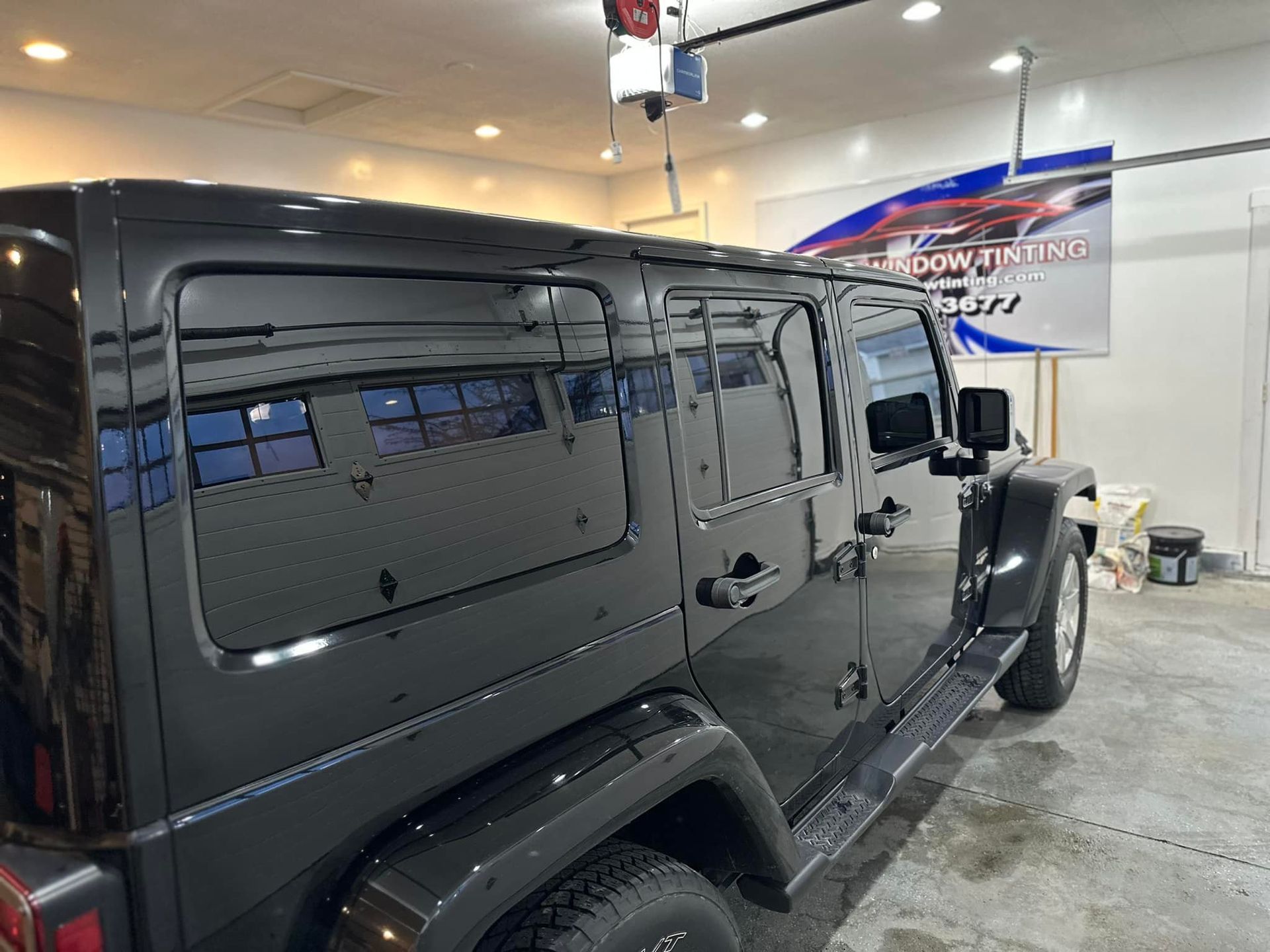 A black jeep is parked in a garage next to a sign.