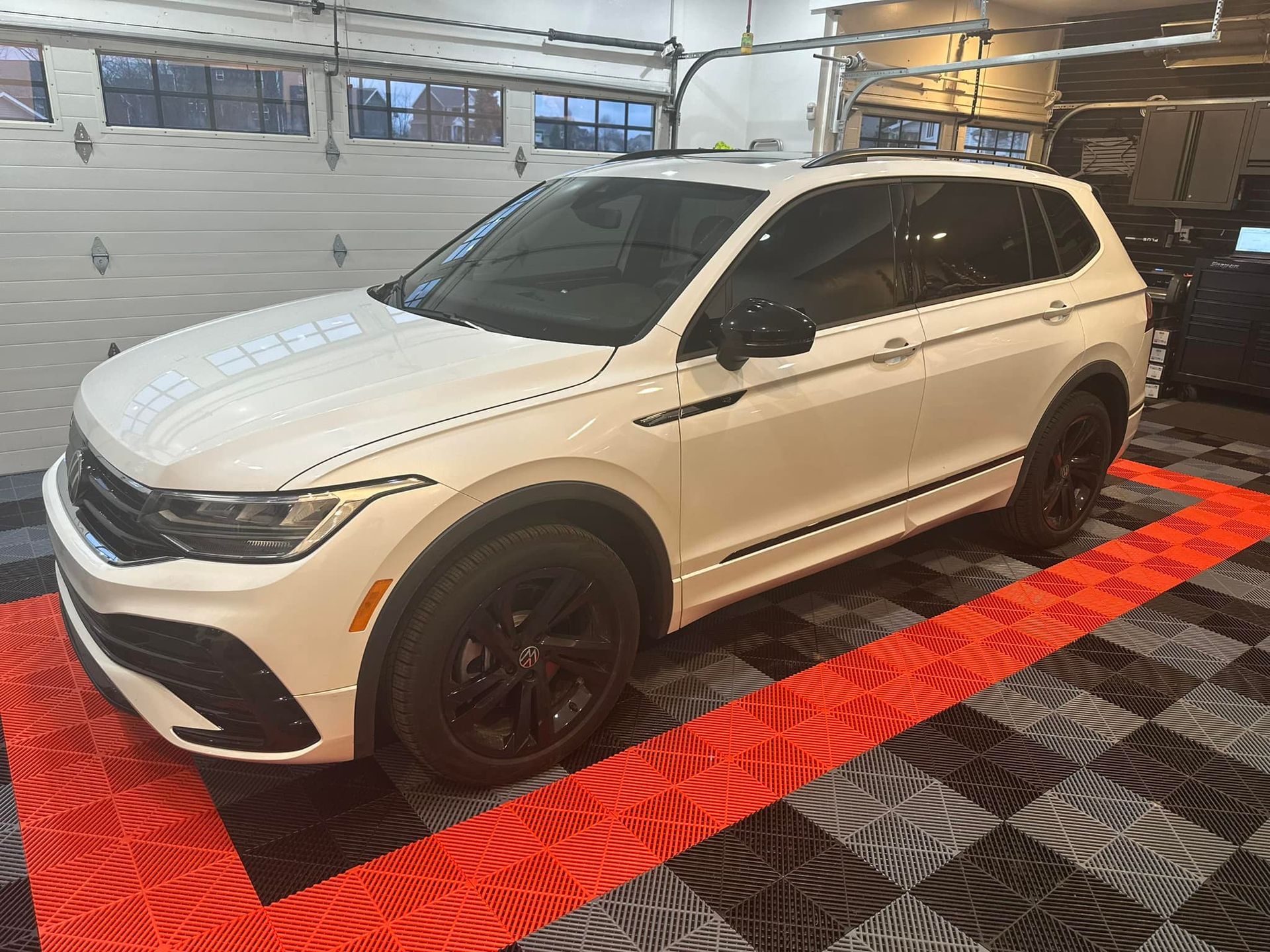 A white suv is parked on a checkered floor in a garage.