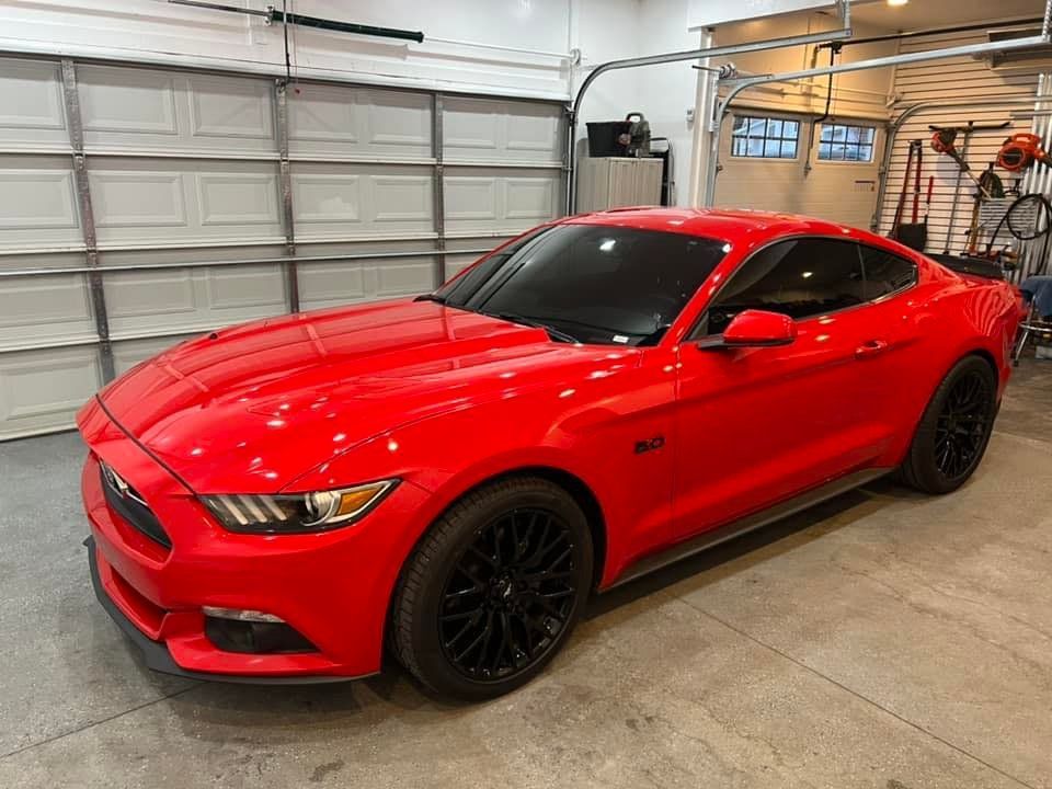 A red mustang is parked in a garage next to a garage door.