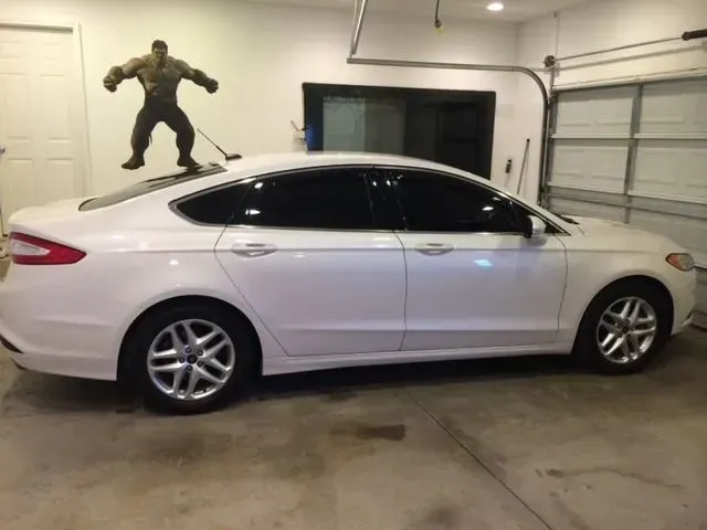 A white car is parked in a garage with a hulk statue on the wall behind it.