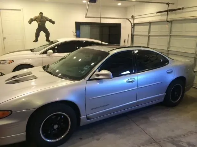A silver car is parked in a garage next to a white car