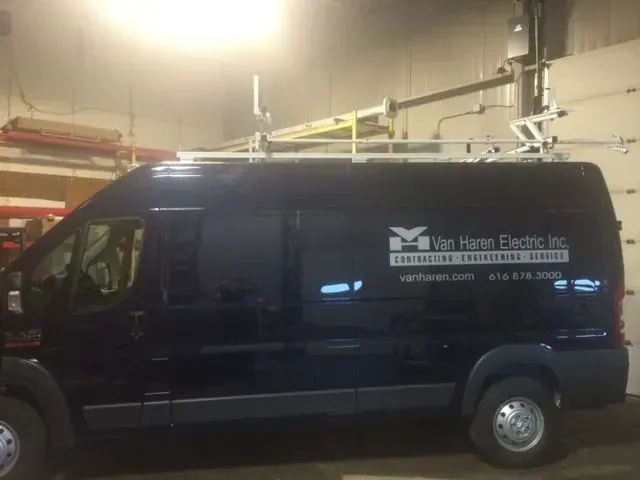 A black van is parked in a garage with a ladder on the roof.