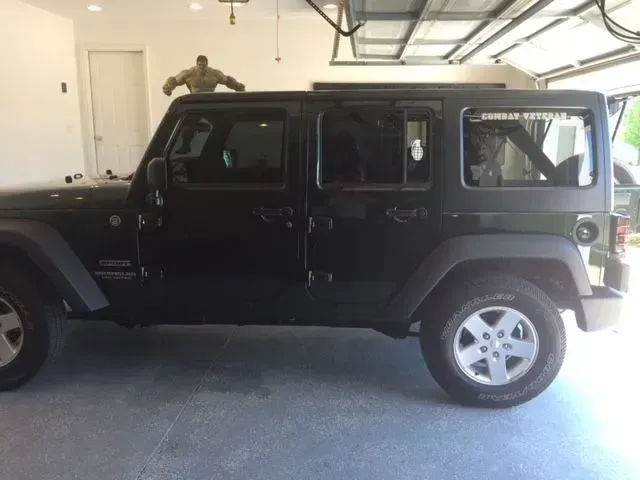 A black jeep is parked in a garage with its doors open.