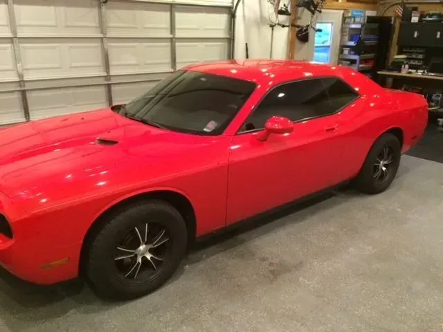 A red dodge challenger is parked in a garage