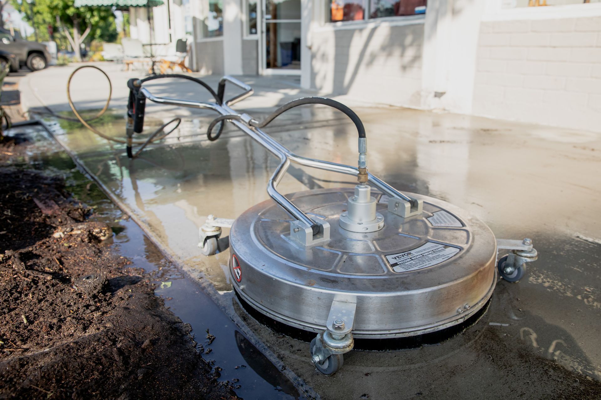 A stainless steel machine is cleaning a concrete driveway.