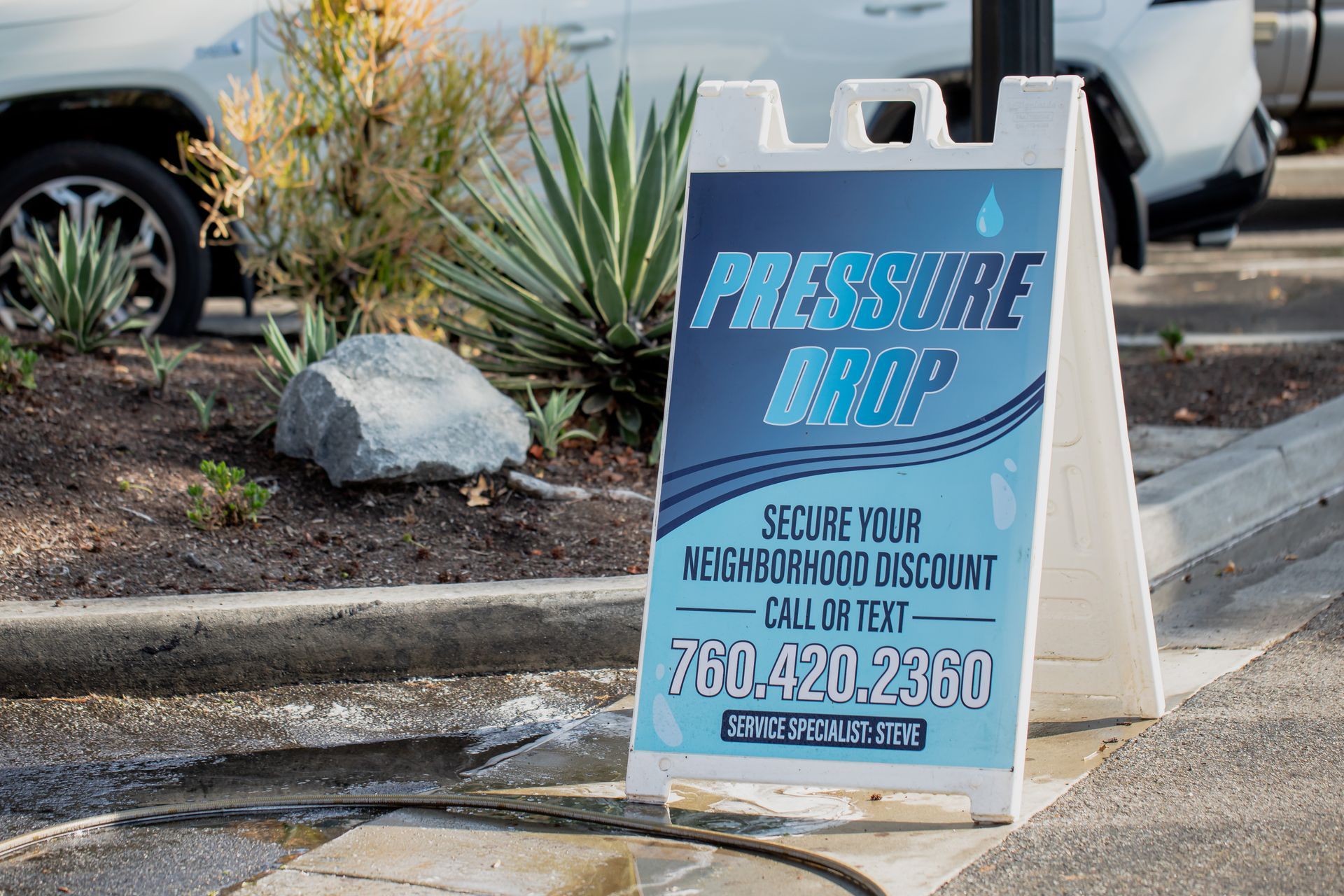 A sign for pressure drop is sitting on the sidewalk next to a car.
