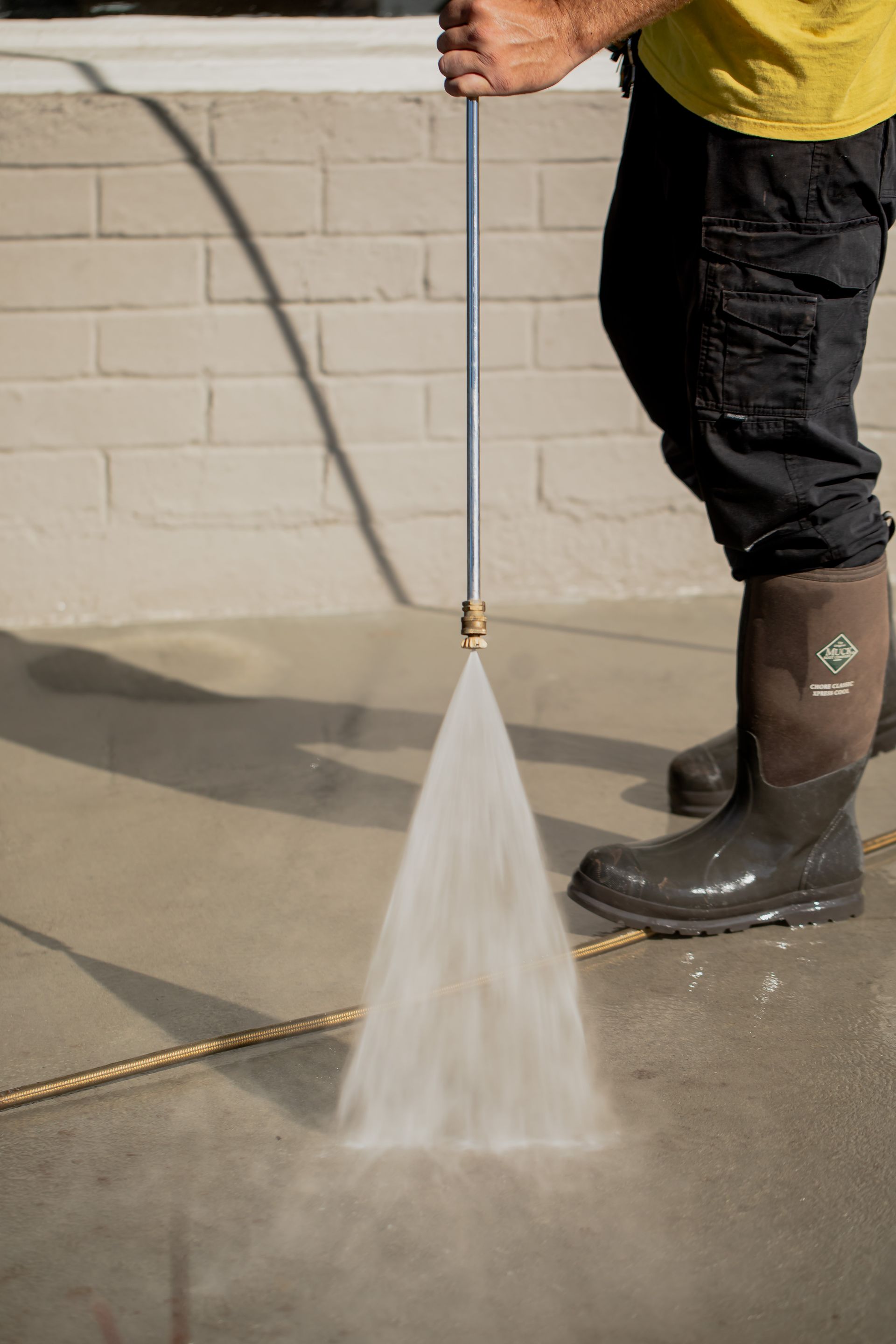 A man is using a high pressure washer to clean a sidewalk.