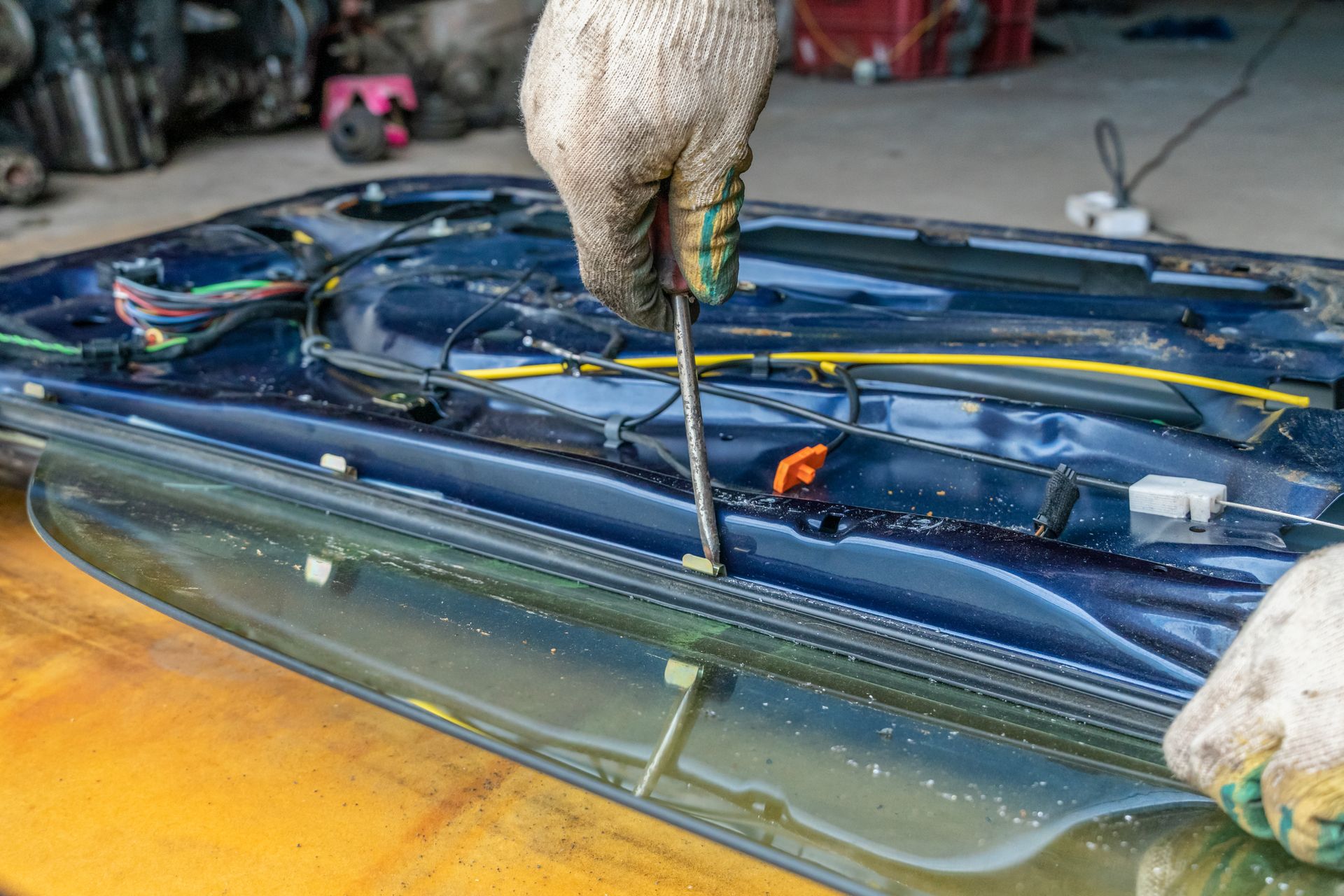 Gloved hands using a tool to pry open a car windshield during repair work