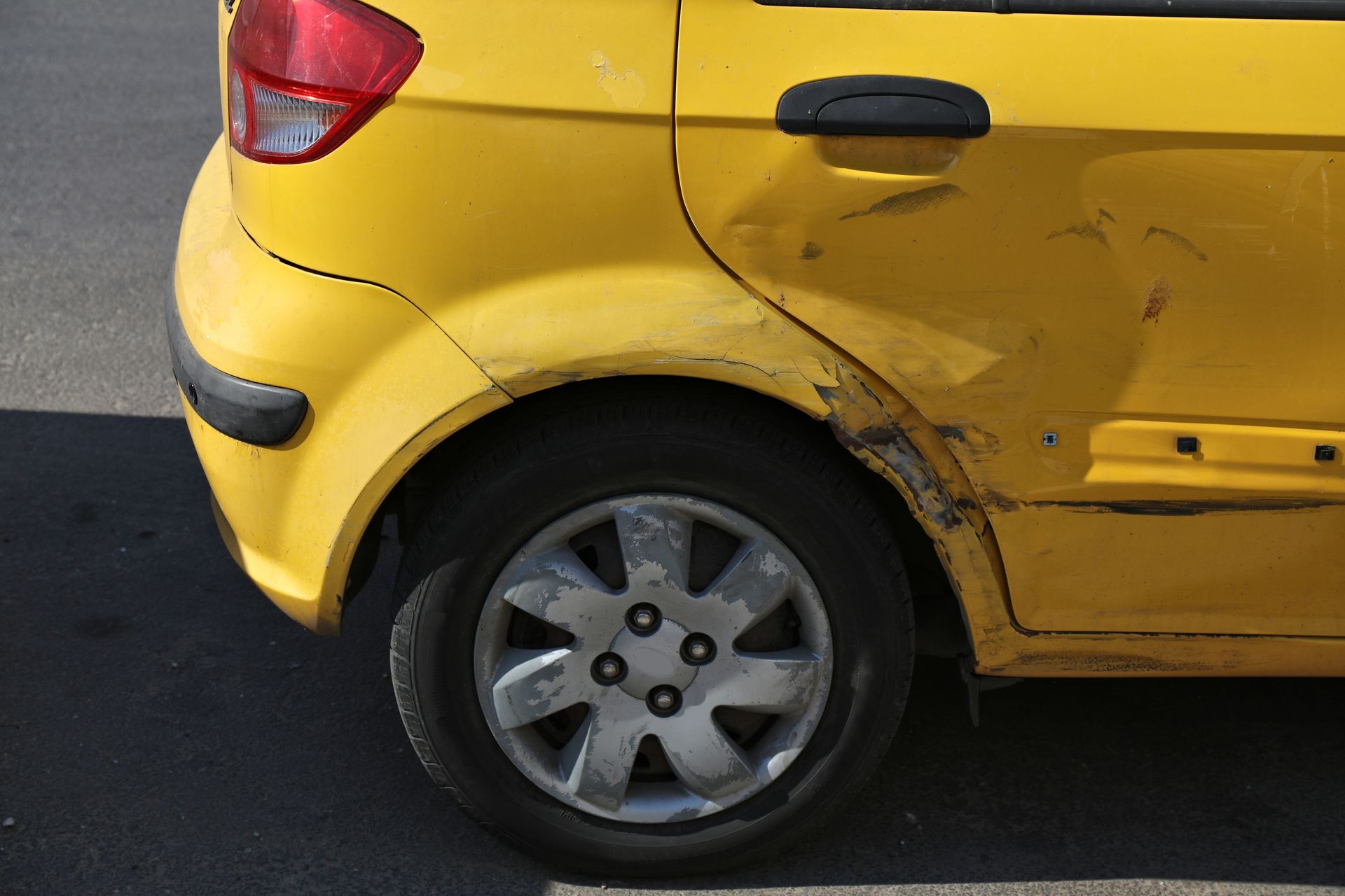 Yellow car with rear-side body damage and scratches near the back wheel