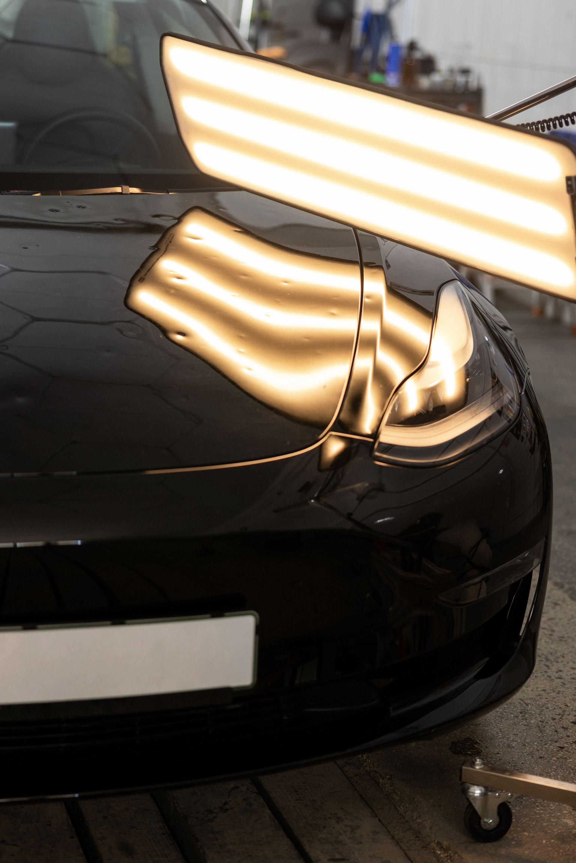 Black car front corner with bright reflections in a garage or workshop