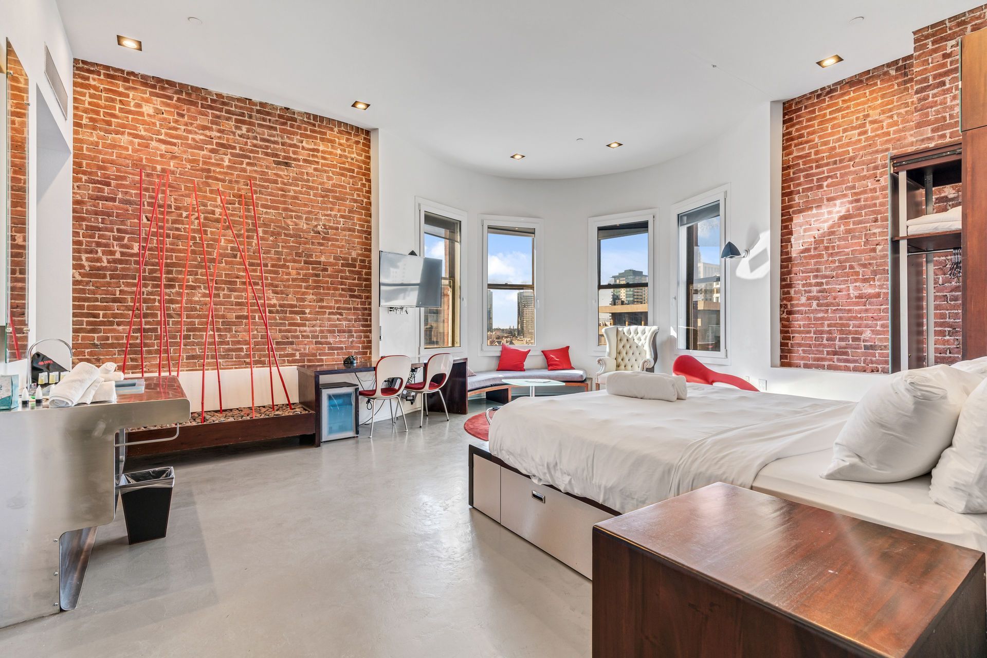 Bedroom with exposed brick walls, curved windows, bed, and seating area.