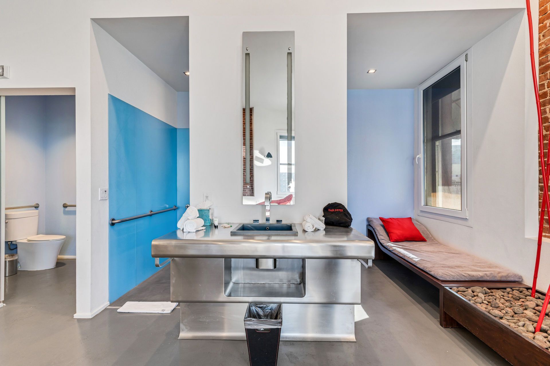 Modern bathroom with stainless steel sink, blue walls, a bench, and a toilet.