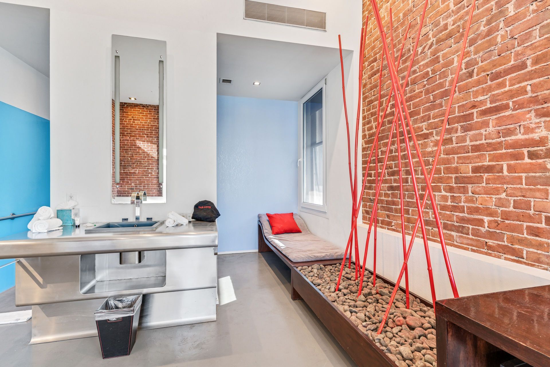 Modern bathroom with red brick wall, red branches, and a bench with a red pillow.