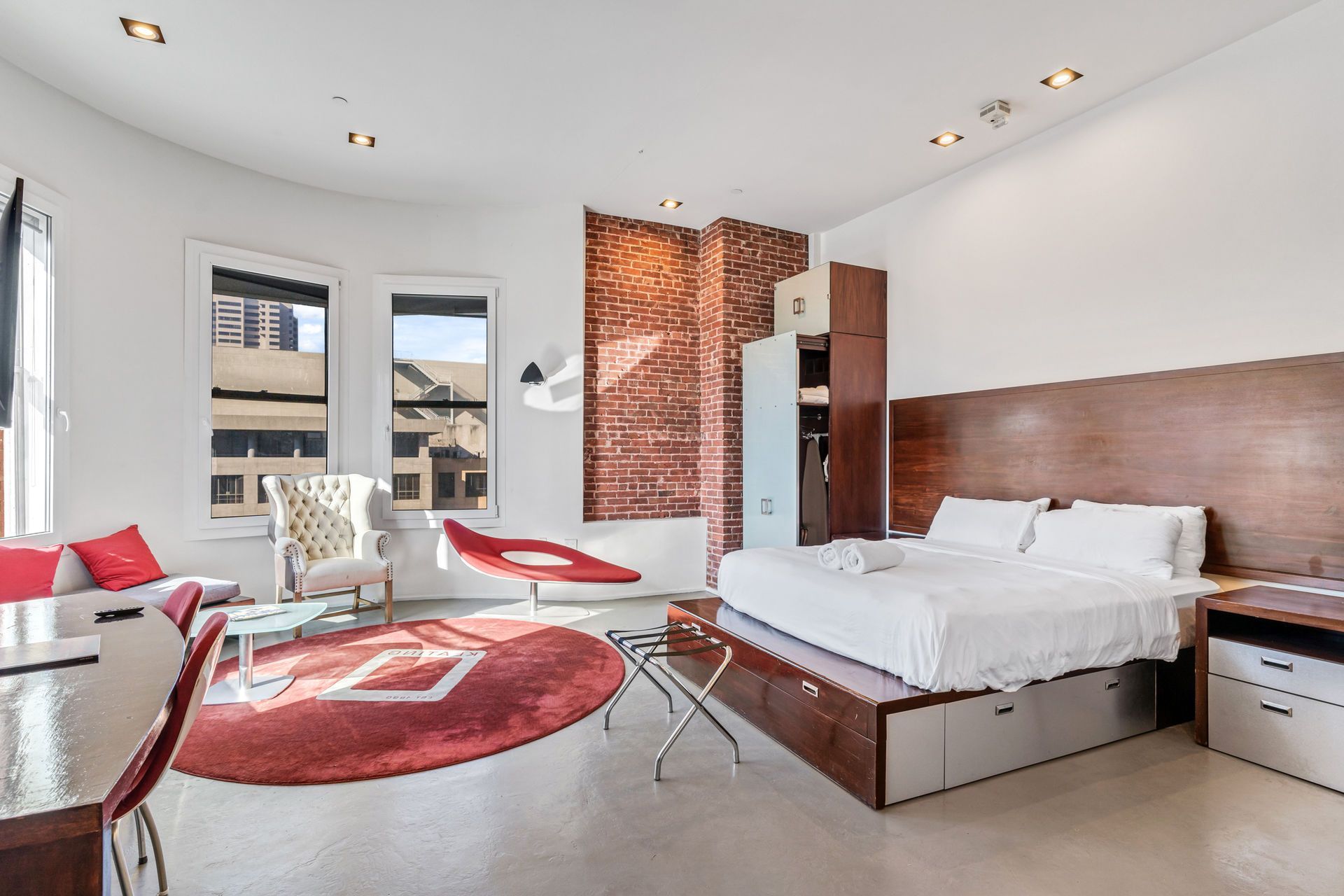 Modern hotel room with a bed, red accents, and brick wall.