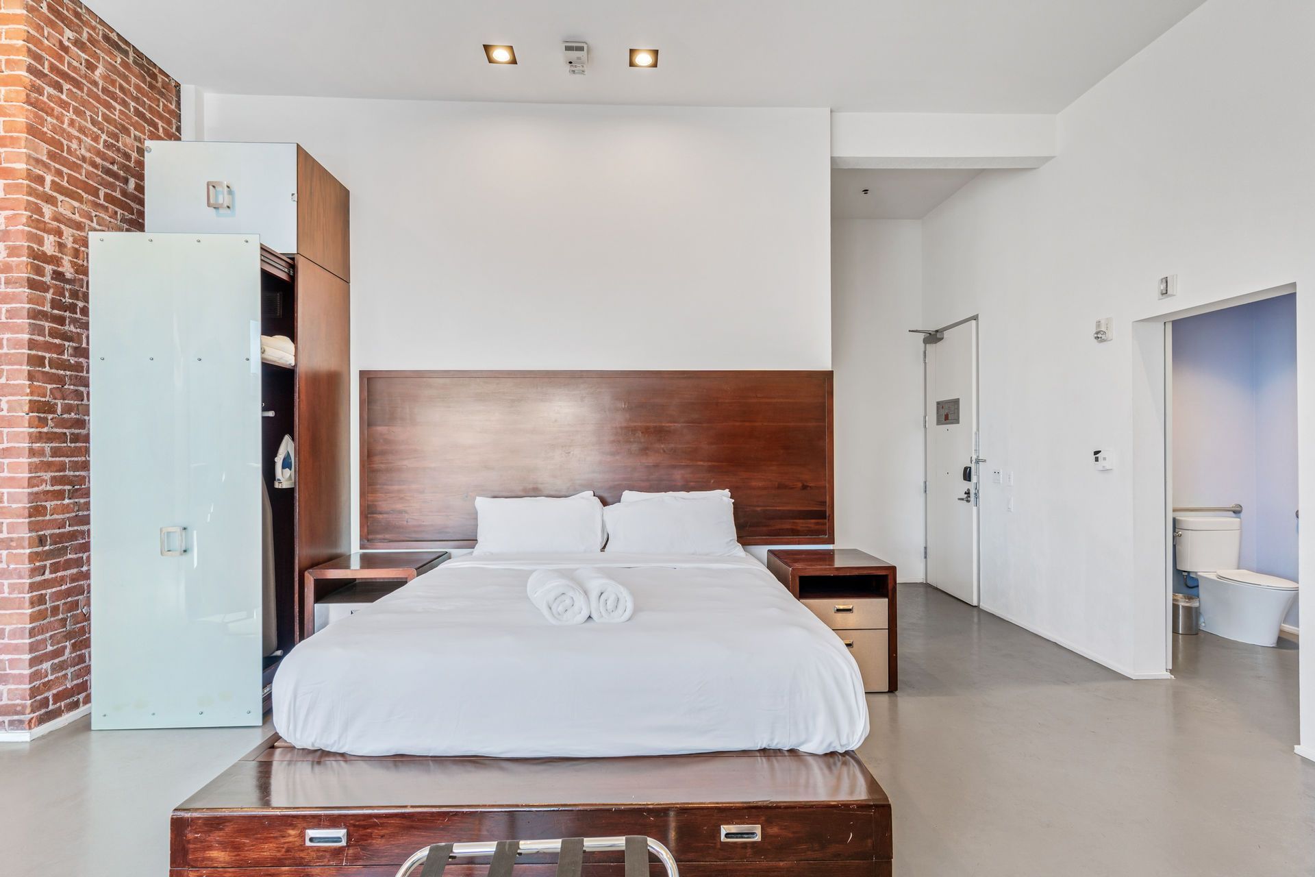 Bedroom with a bed on a wooden platform, wooden headboard, and storage closets. A brick wall is visible.