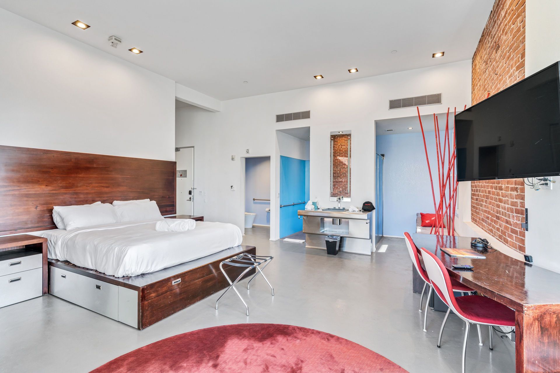 Hotel room with bed, desk, exposed brick wall, and modern decor.