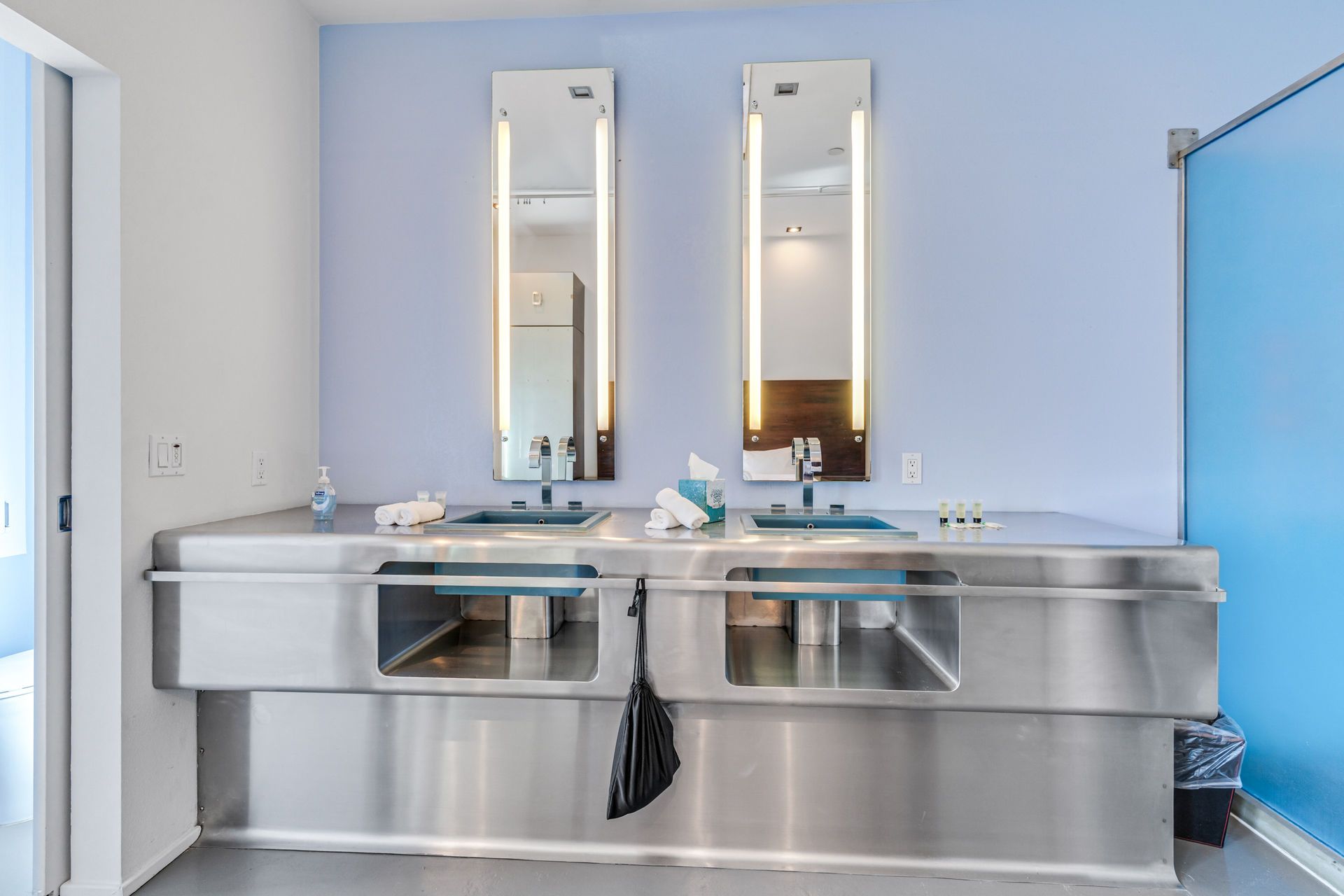 Modern bathroom with stainless steel double sink and mirrors on a light blue wall.