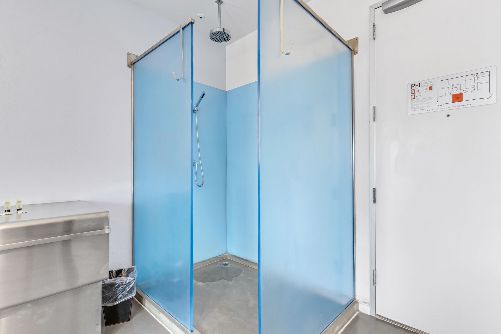 A shower stall with light blue walls and glass doors. A stainless steel sink is to the left.