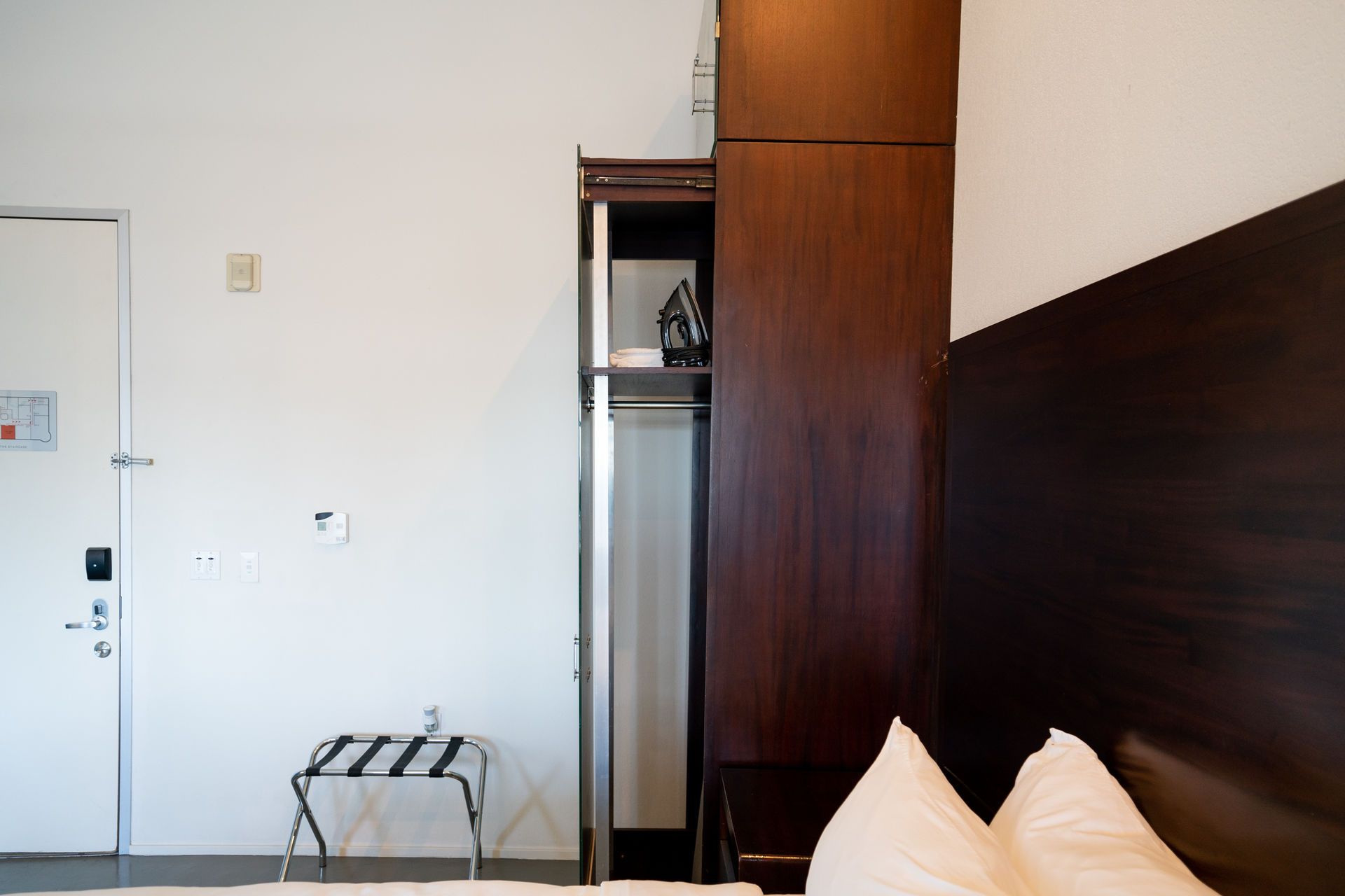 Interior view of a hotel room with a closet, door, and a bed with white pillows.