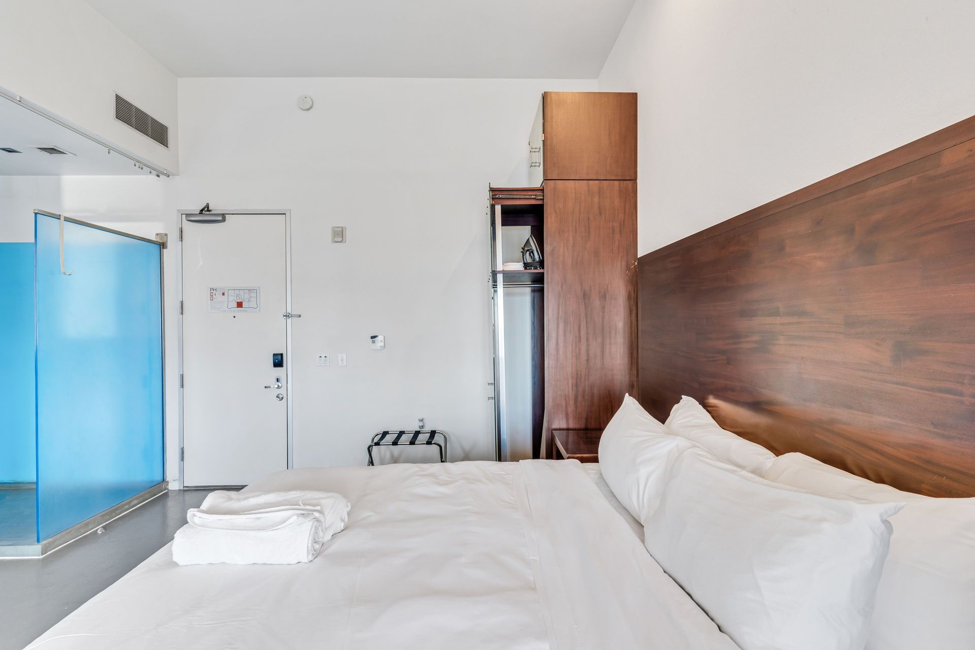 Hotel room with a large bed, wooden headboard, and blue glass shower enclosure.
