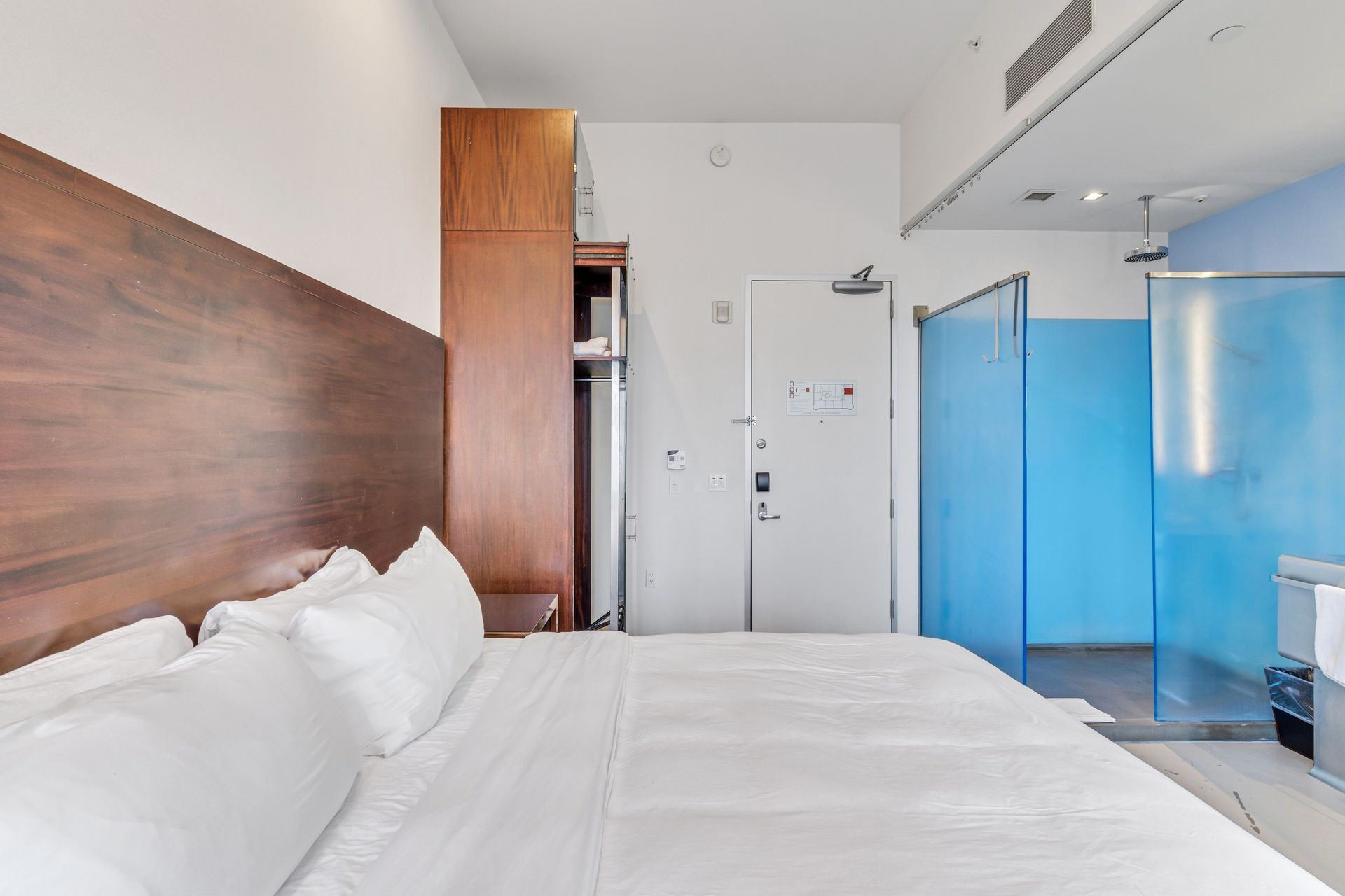 Bedroom with large bed, wooden headboard, closet, door, and blue-tinted shower area.