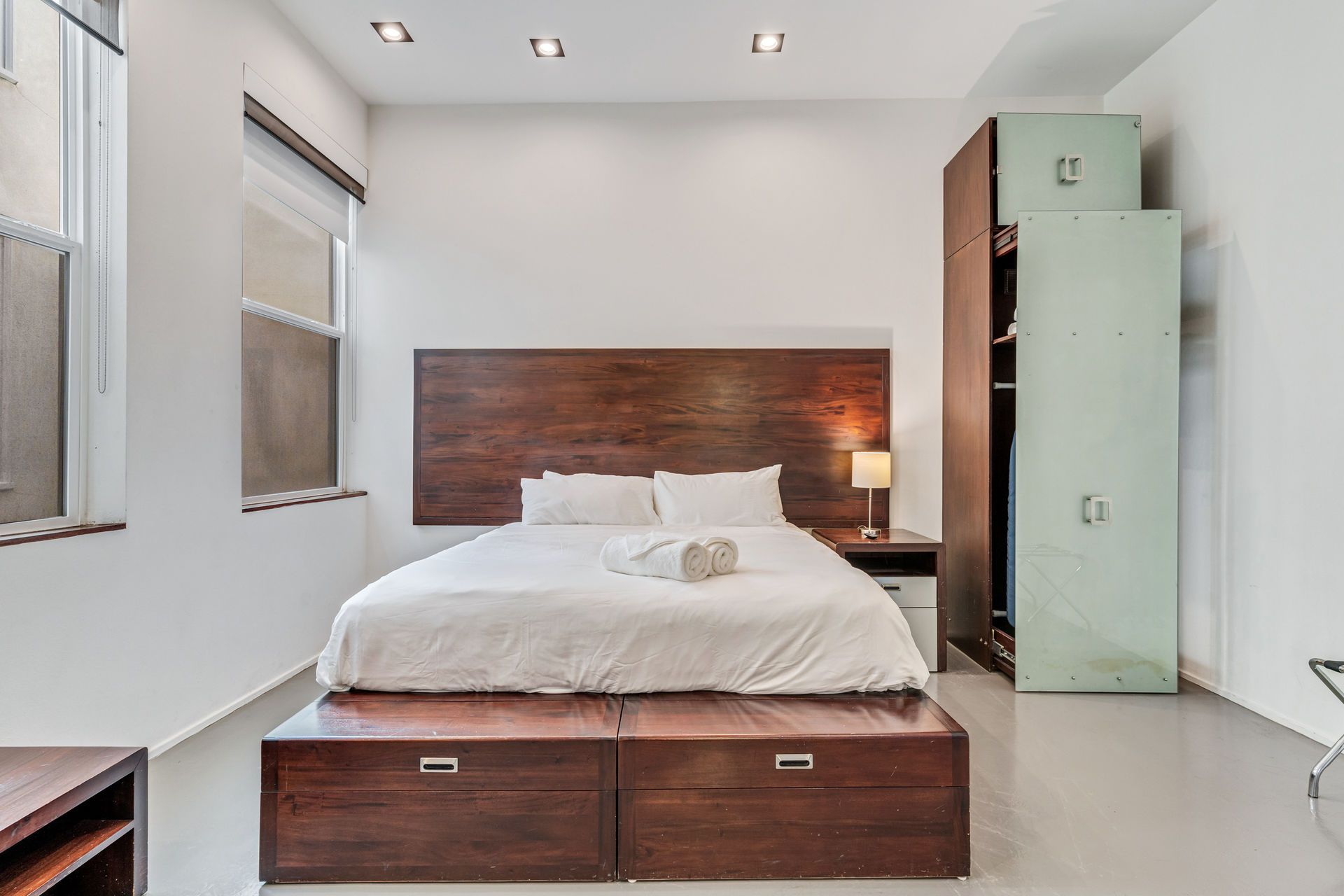 Bedroom with wooden bed frame, large headboard, white bedding, and tall wardrobe.
