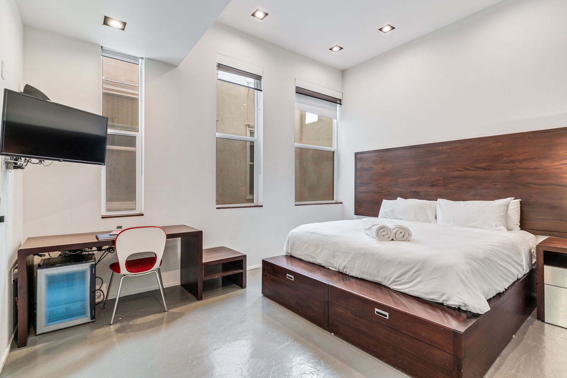 Modern hotel room with king bed, desk, and small fridge.