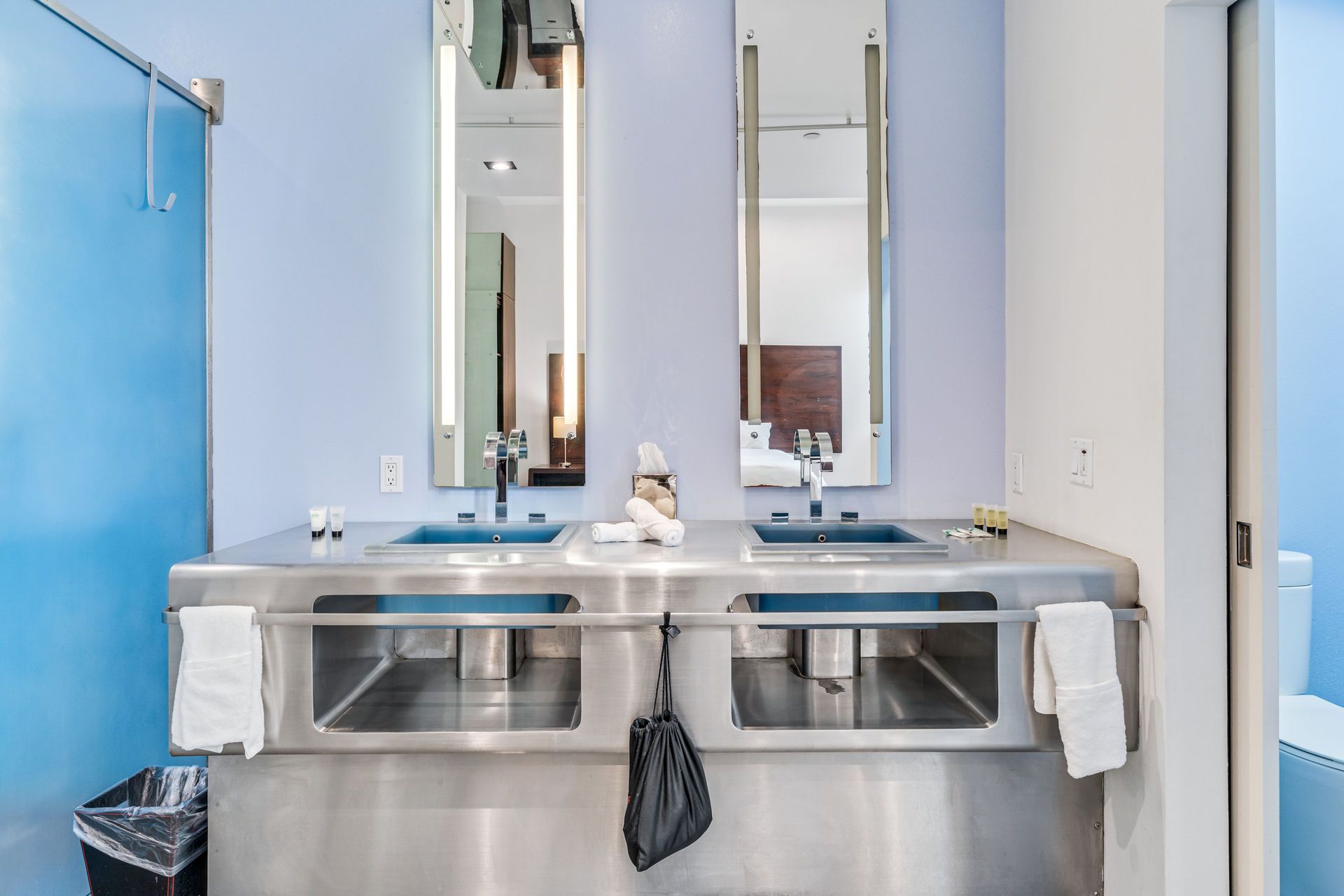 Double sink bathroom with stainless steel countertop and light blue walls.