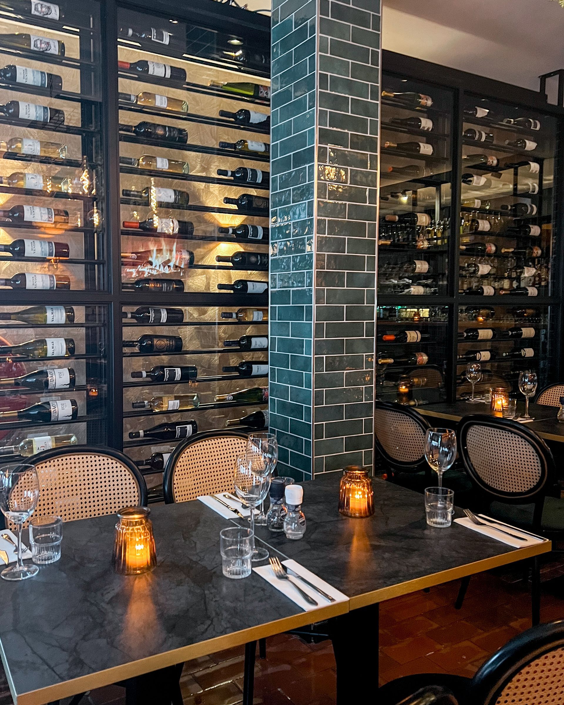 Een restaurant met tafels en stoelen en een muur vol wijnflessen.