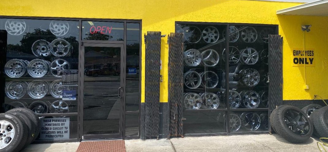 Exterior of a tire shop with wheels displayed in windows, yellow building.