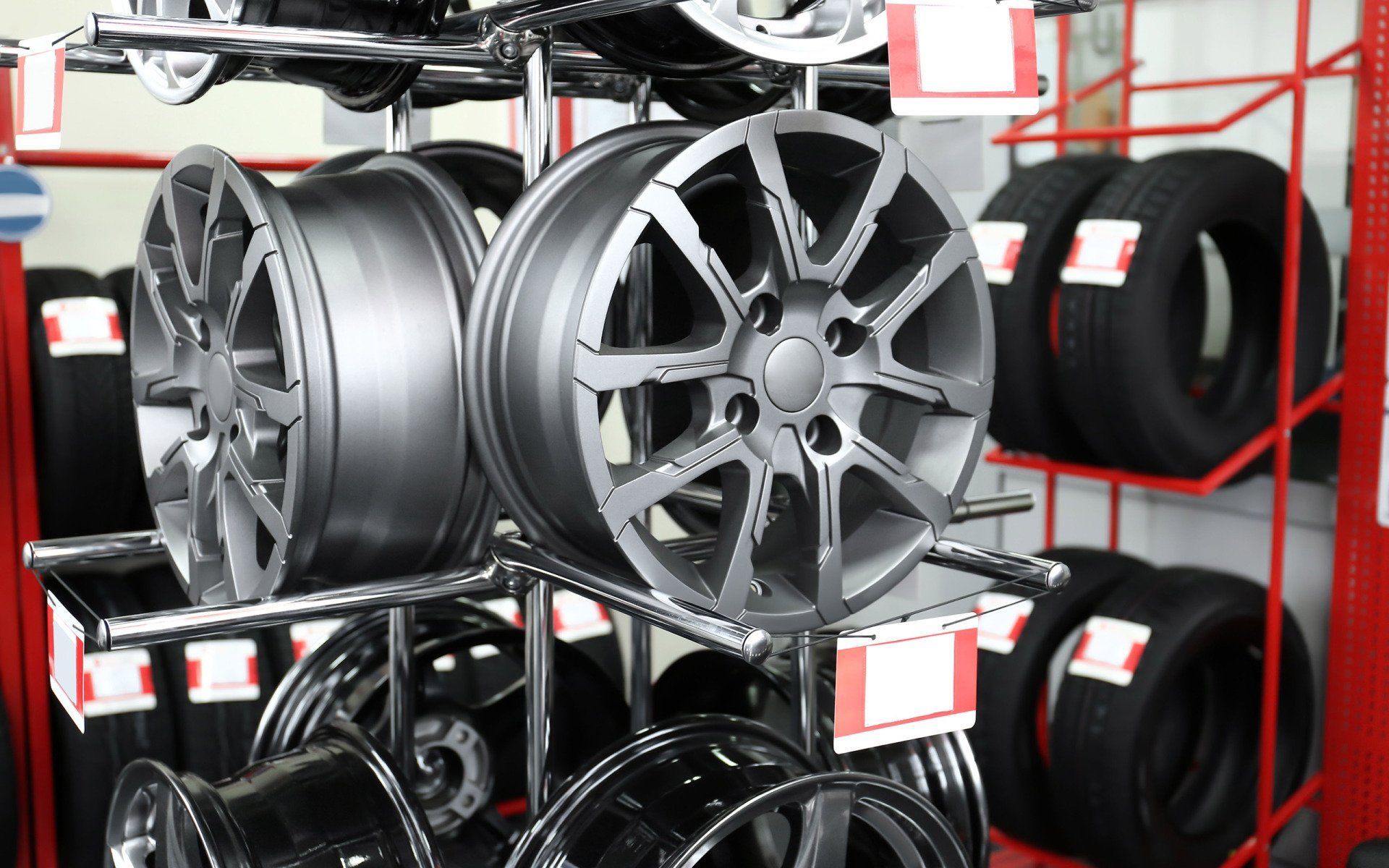 Car wheels and tires displayed on a metal rack in an auto parts store.