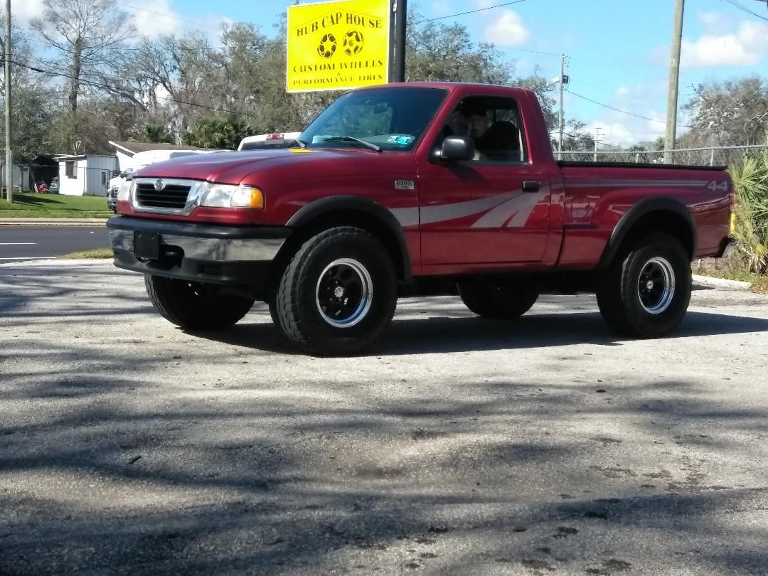 Red Mazda pickup truck parked outside a business on a sunny day.
