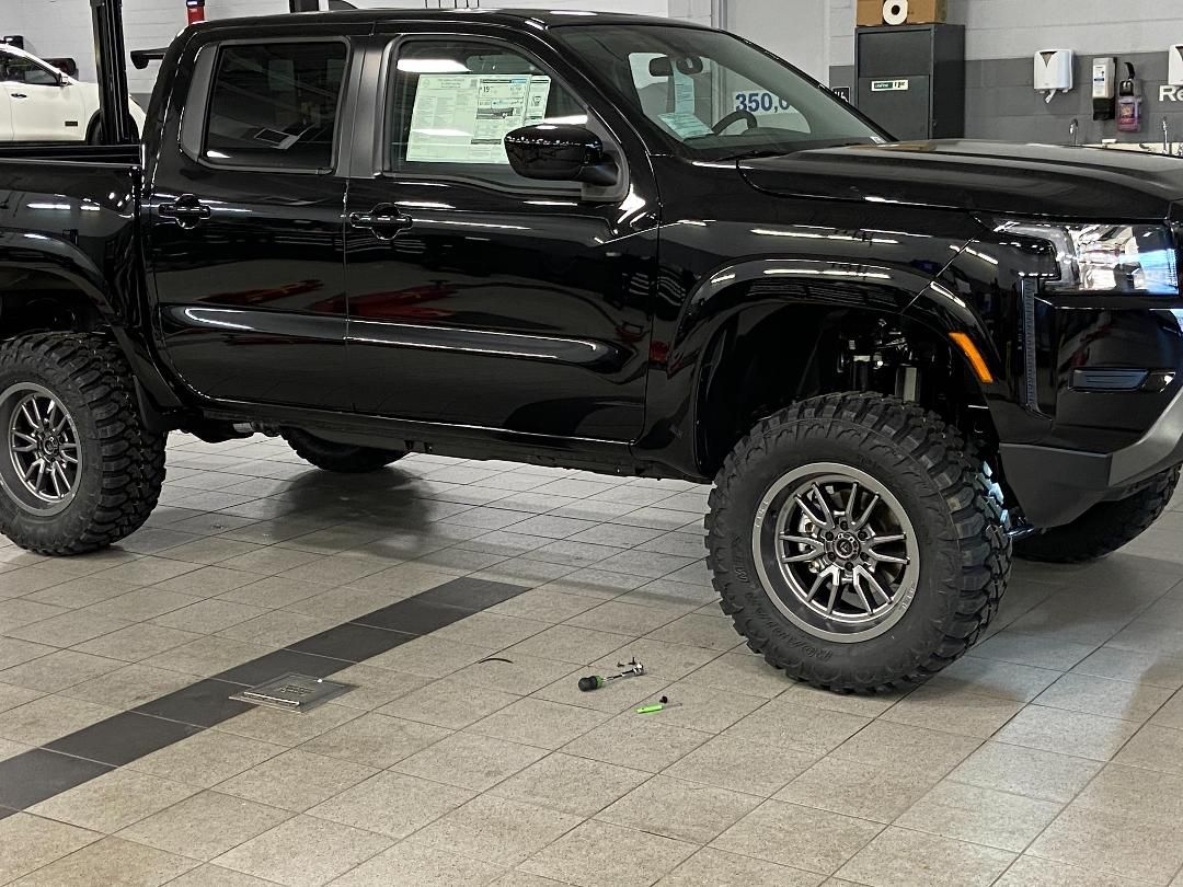 Black lifted pickup truck inside a garage with large, off-road tires.