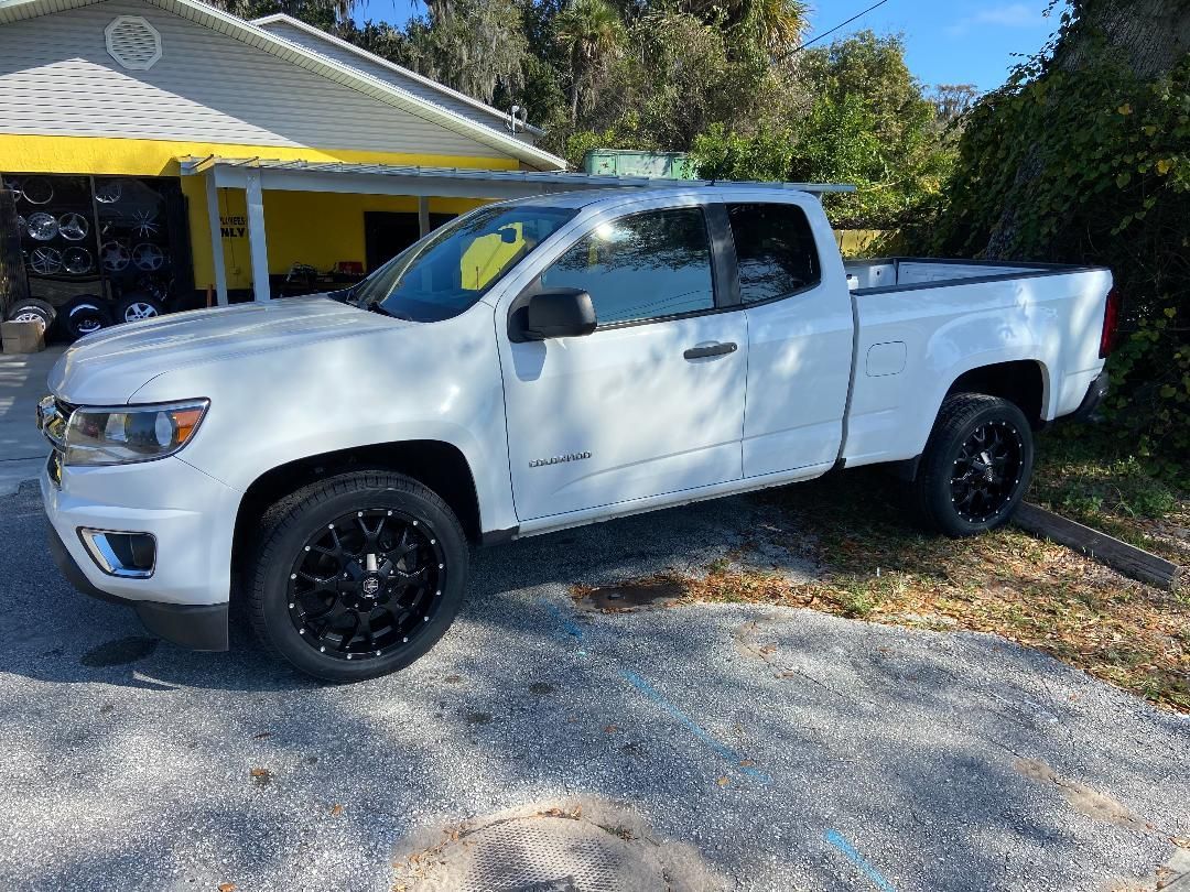 White Chevrolet Colorado pickup truck parked near a building with a yellow awning. Black wheels.
