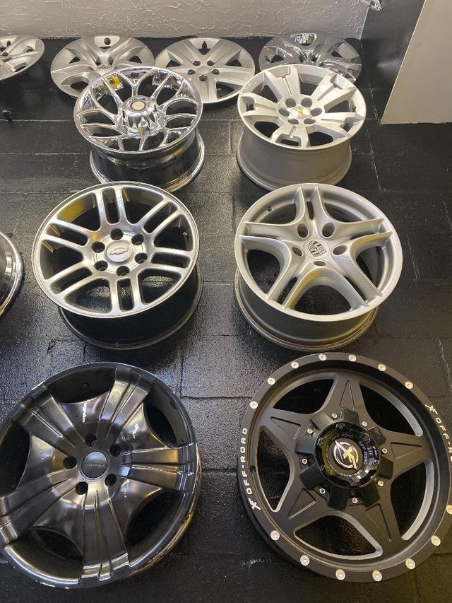 Assortment of car rims in various styles and colors, displayed on a surface.