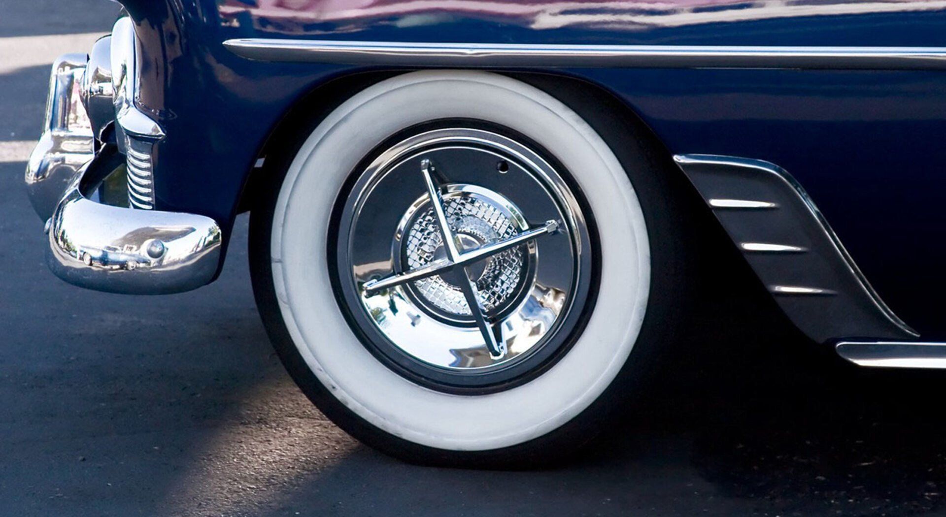 White-walled tire and chrome hubcap on a classic blue car, near front fender.