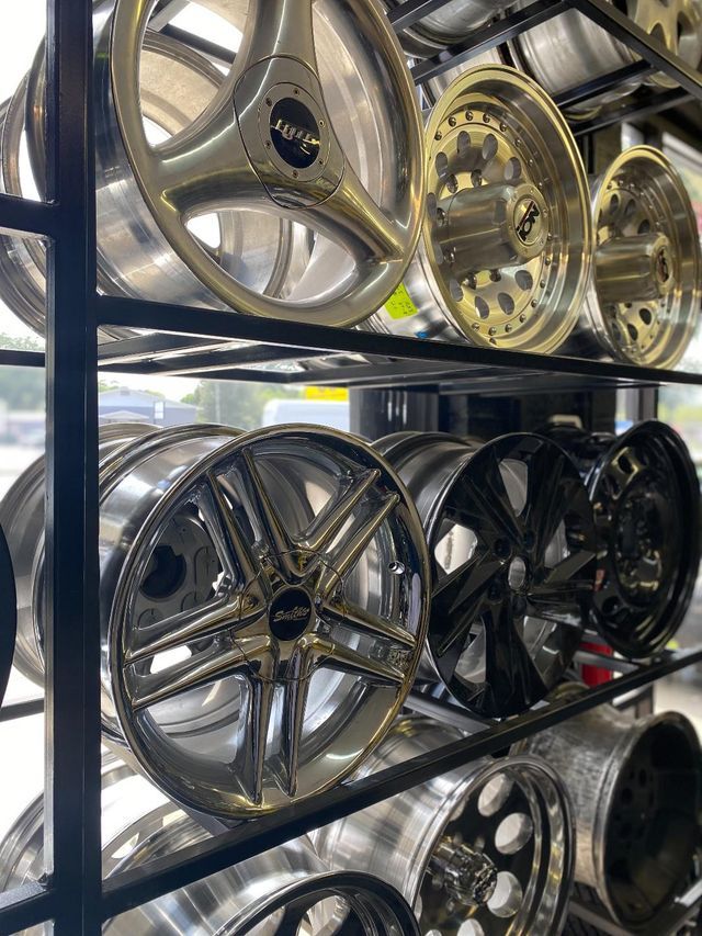 A rack of shiny car rims in silver, chrome, and black, displayed at a store.