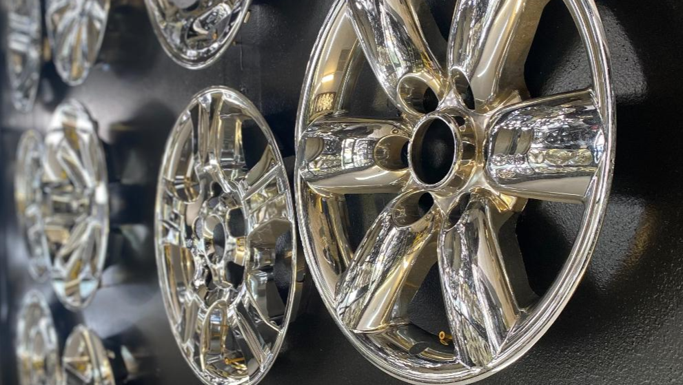 Chrome car wheels hanging on a black wall, reflecting light.
