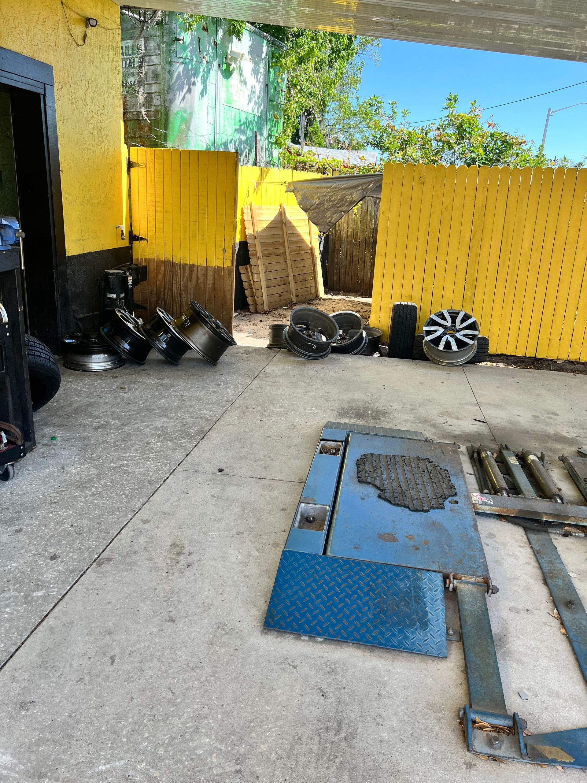 Entrance to a yellow auto repair shop. A lift, tires, and scrap metal are visible on the concrete.