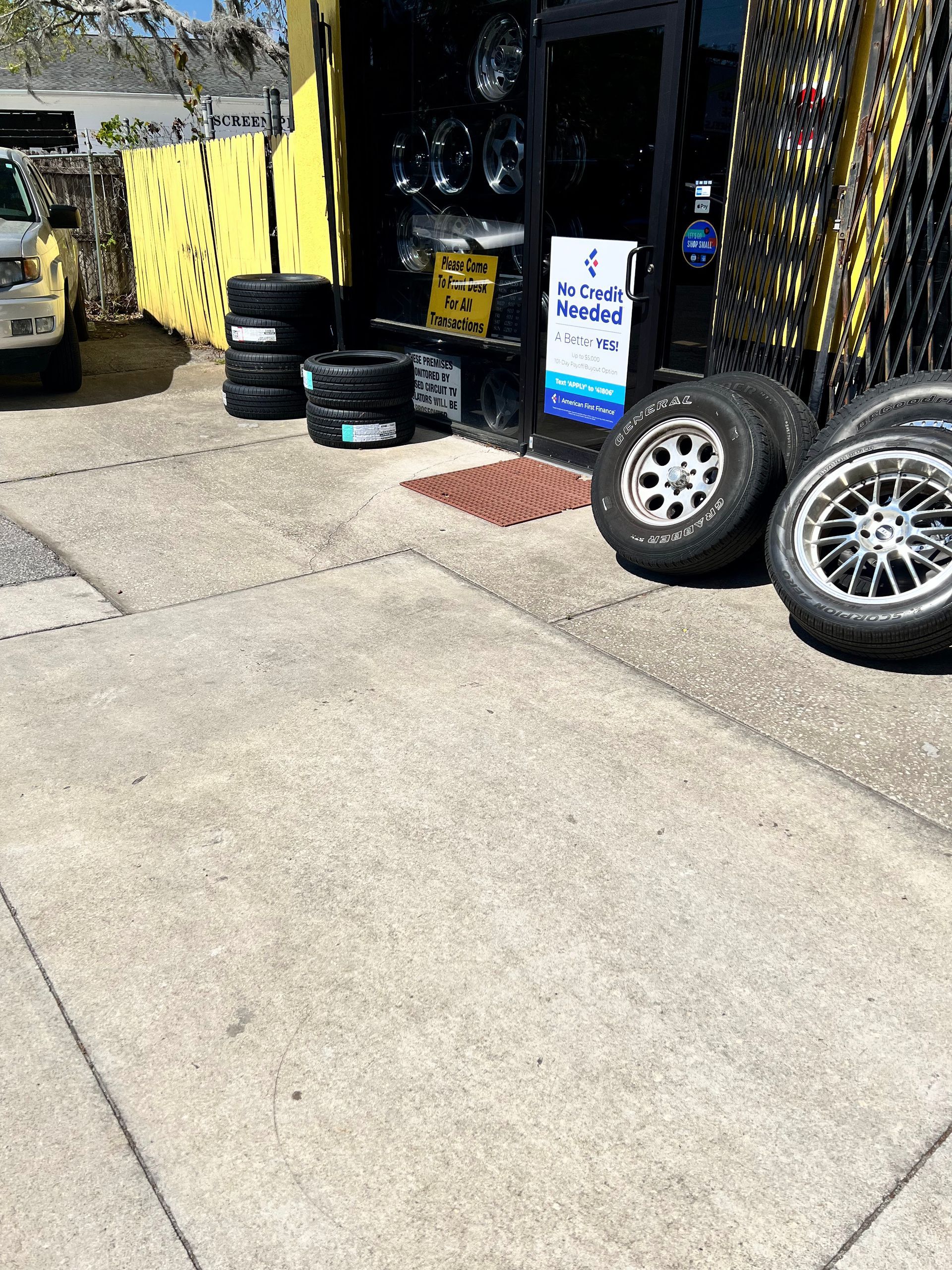 Tires displayed outside a shop, with a concrete sidewalk in front.