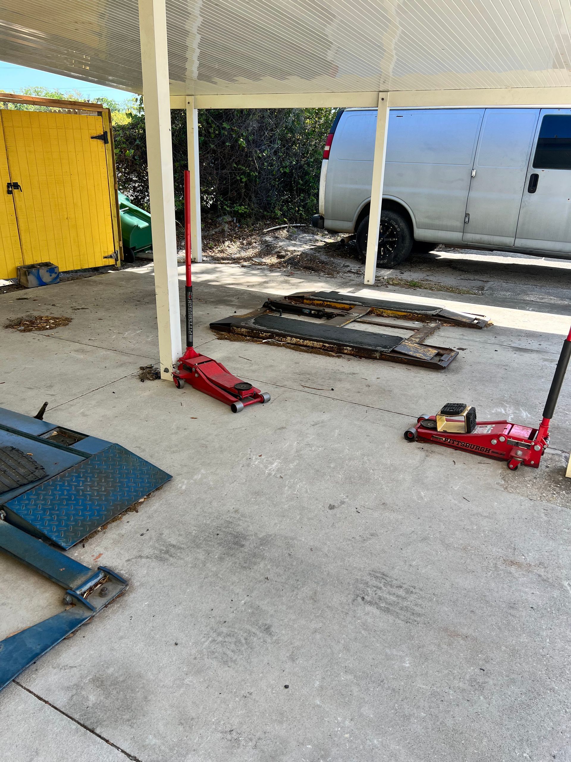 A concrete garage with a red jack, car lift and white van.