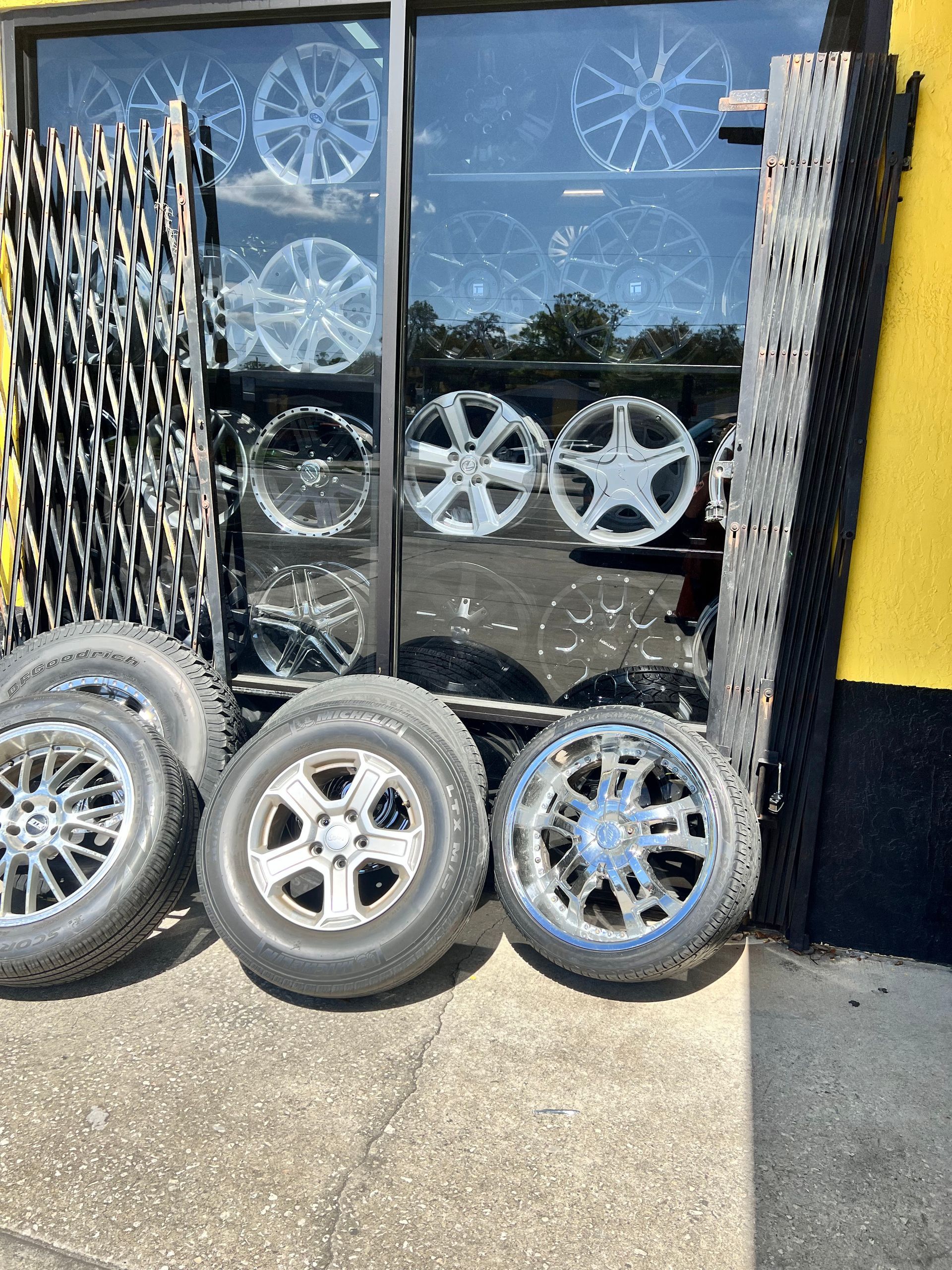 Tires and wheels displayed outside a store with a glass window showcasing various wheel designs.