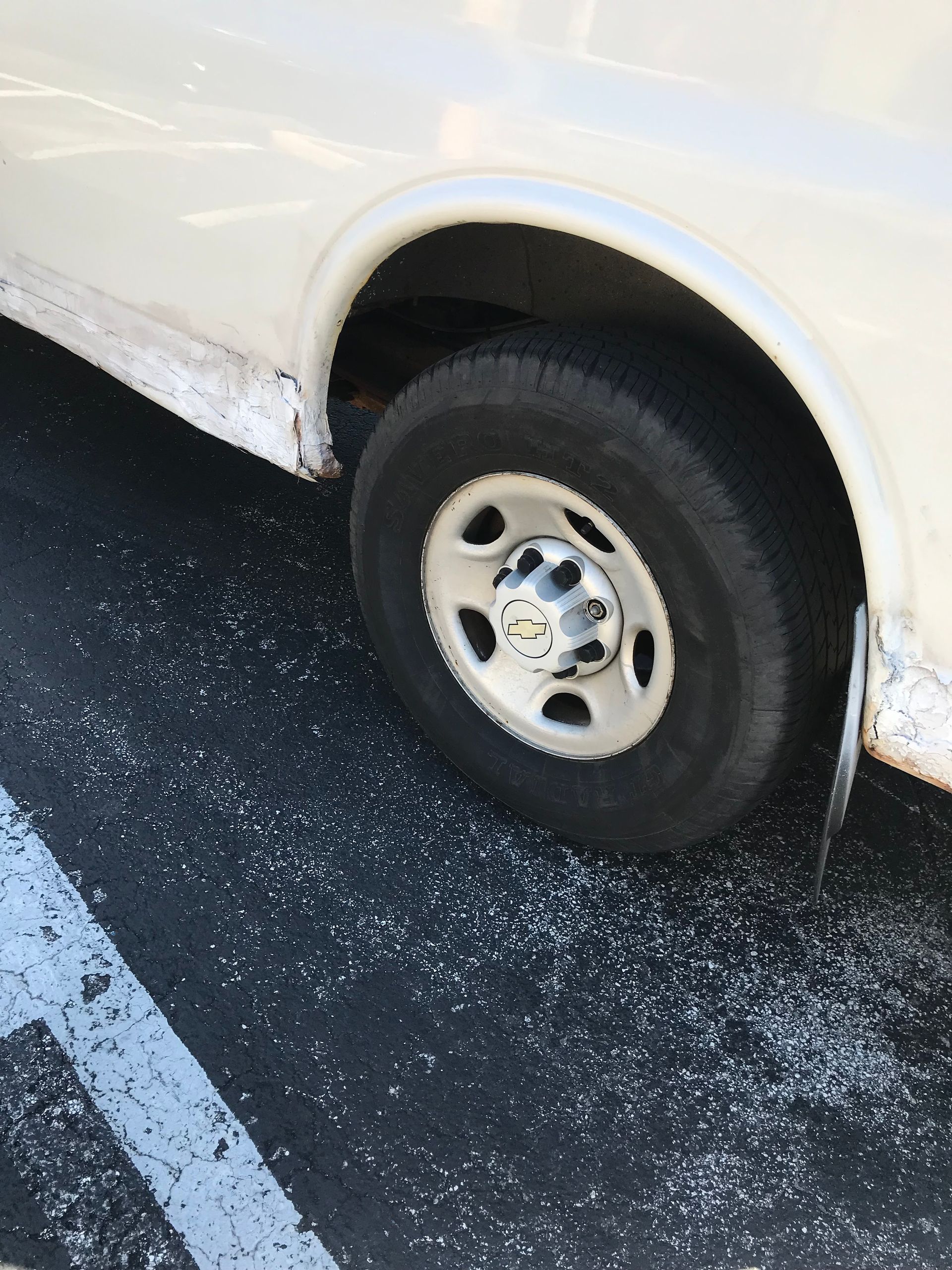 White van's rear wheel, parked on asphalt with white markings, surrounded by scattered white substance.