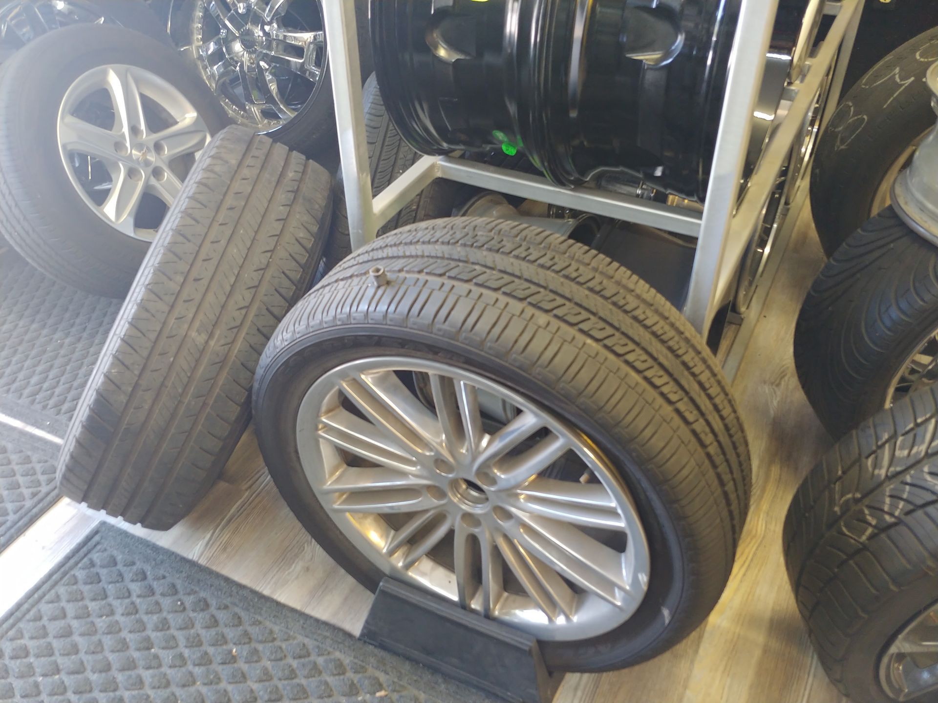 Tires on rims in a shop, various sizes, silver and black, some stacked, indoors.