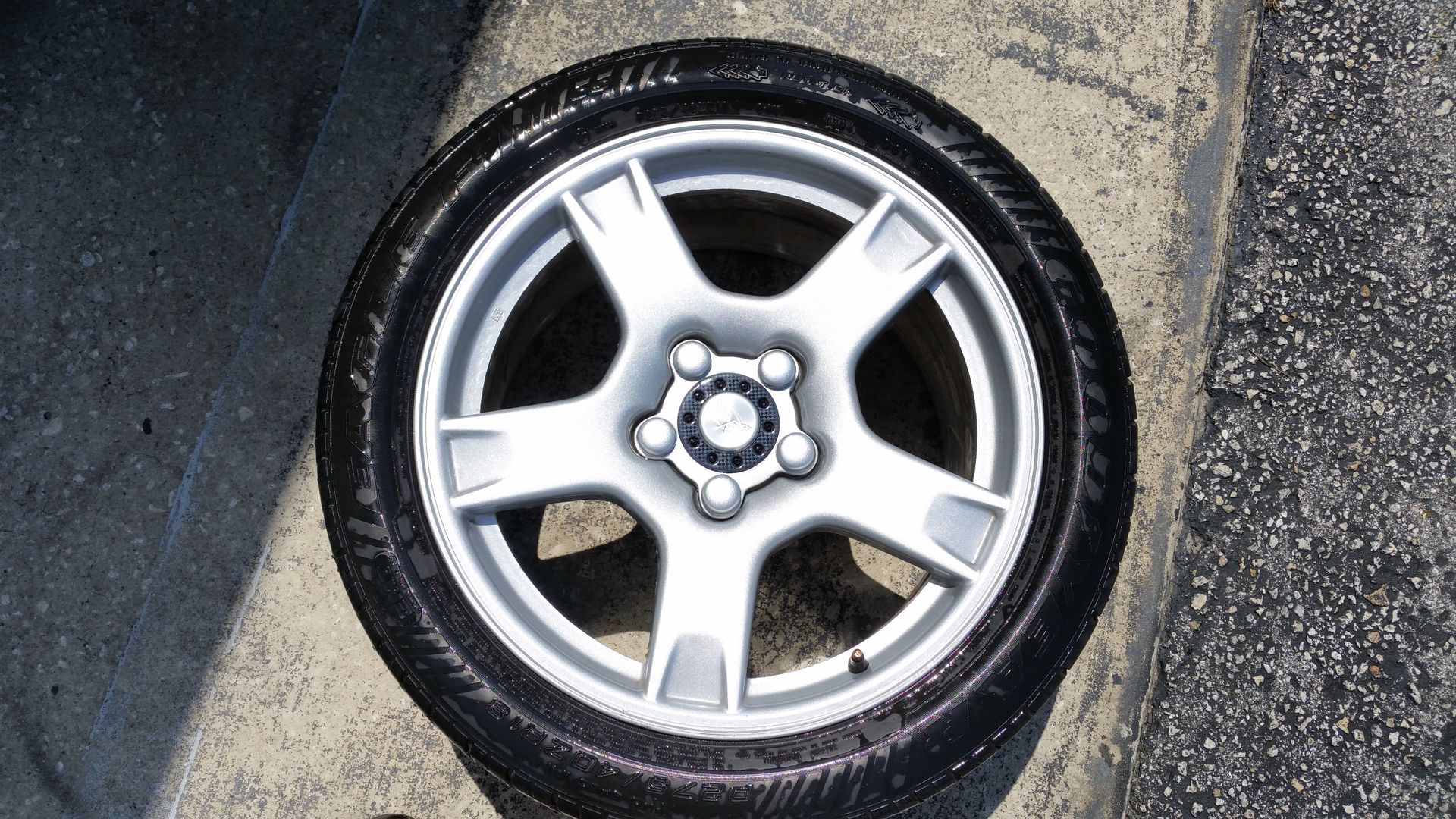 Silver car wheel with black tire on a concrete surface.