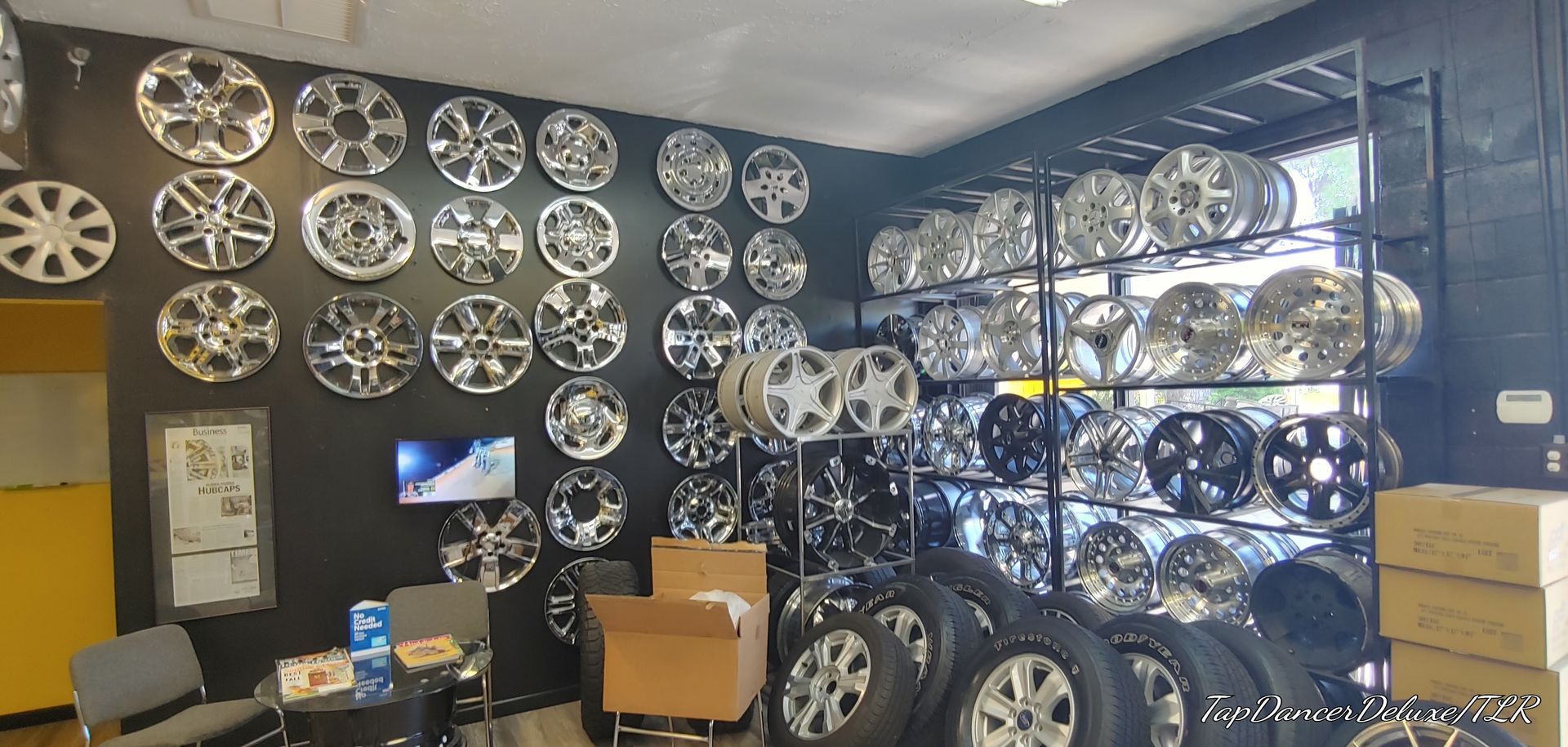 A tire shop interior, with rows of chrome hubcaps on display, shelves of rims, and tires on the floor.